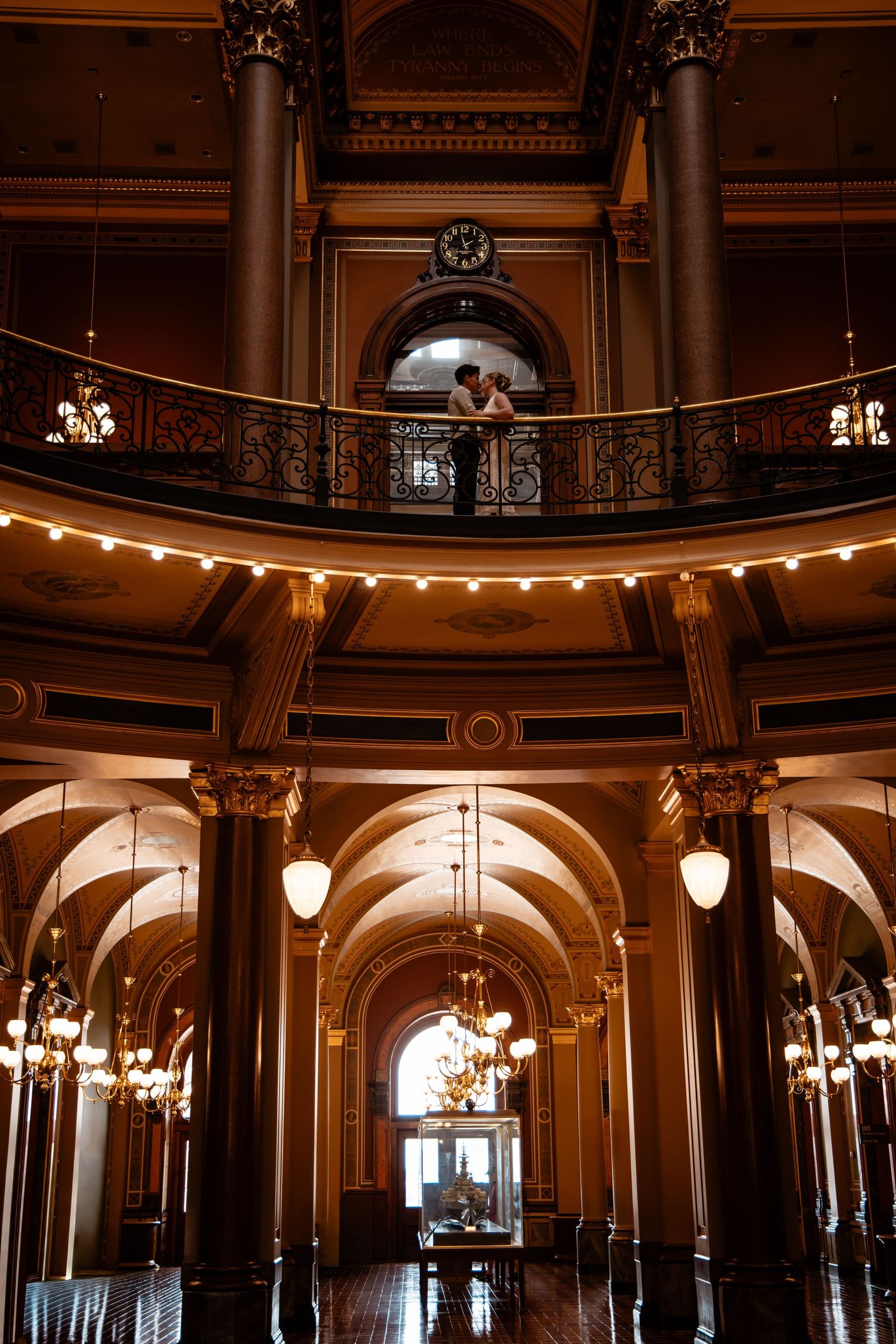 Couple sharing a romantic moment on an ornate balcony inside a grand historic building with arched hallways.