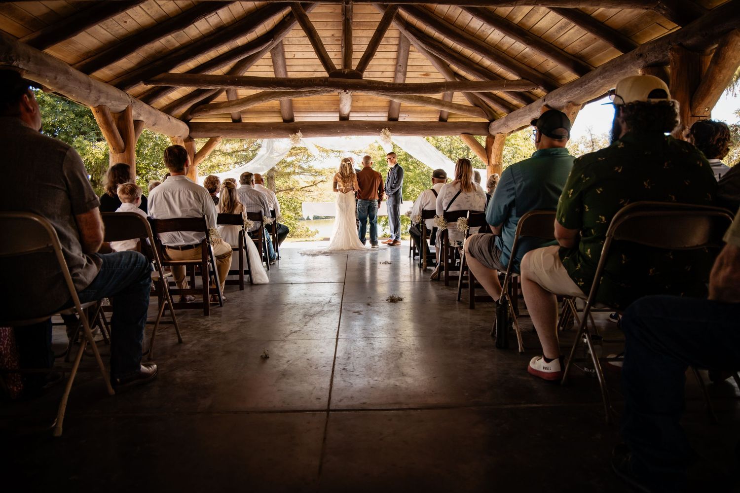 Guests seated in rustic open-air pavilion wedding ceremony with couple at altar.