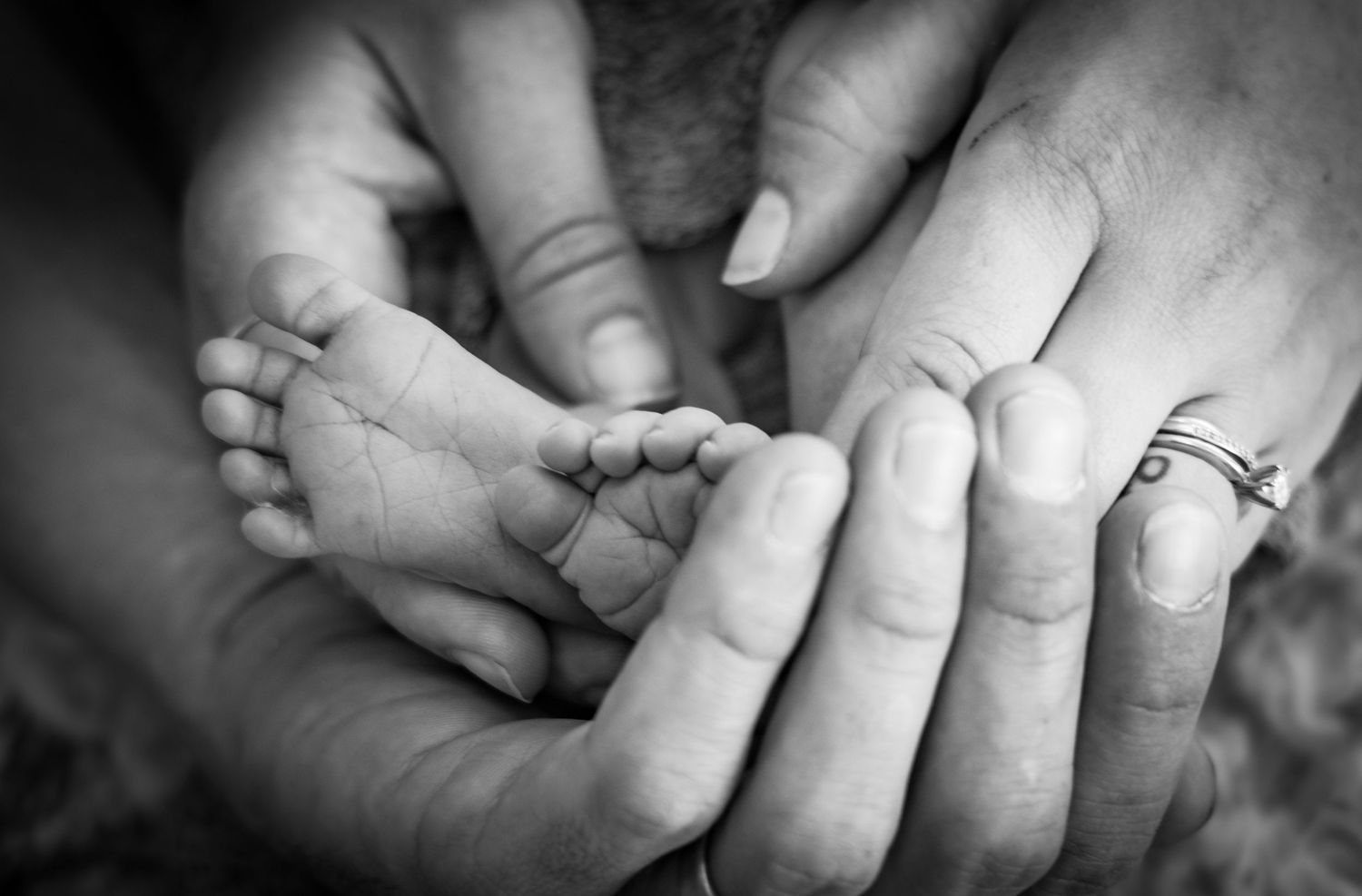Black and white photo of parents cradling newborn baby feet in their hands, symbolizing family love.