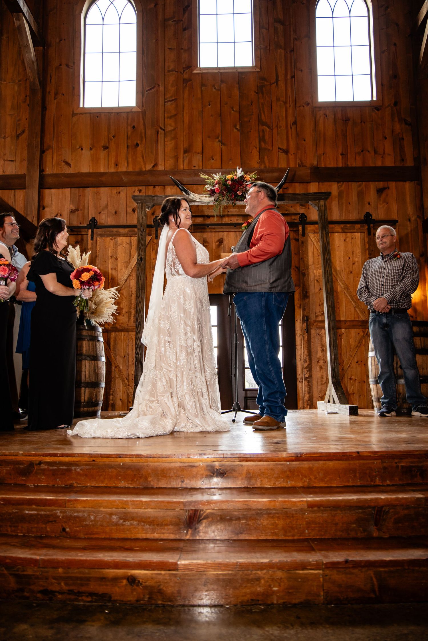 Bride and groom hold hands at the altar inside a rustic barn wedding ceremony.