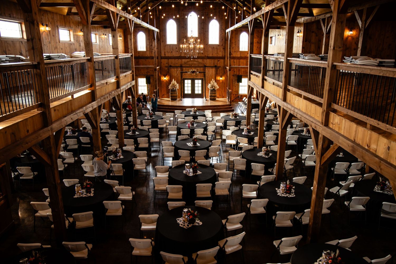 Elegant barn wedding venue with black round tables and warm string lights overhead.