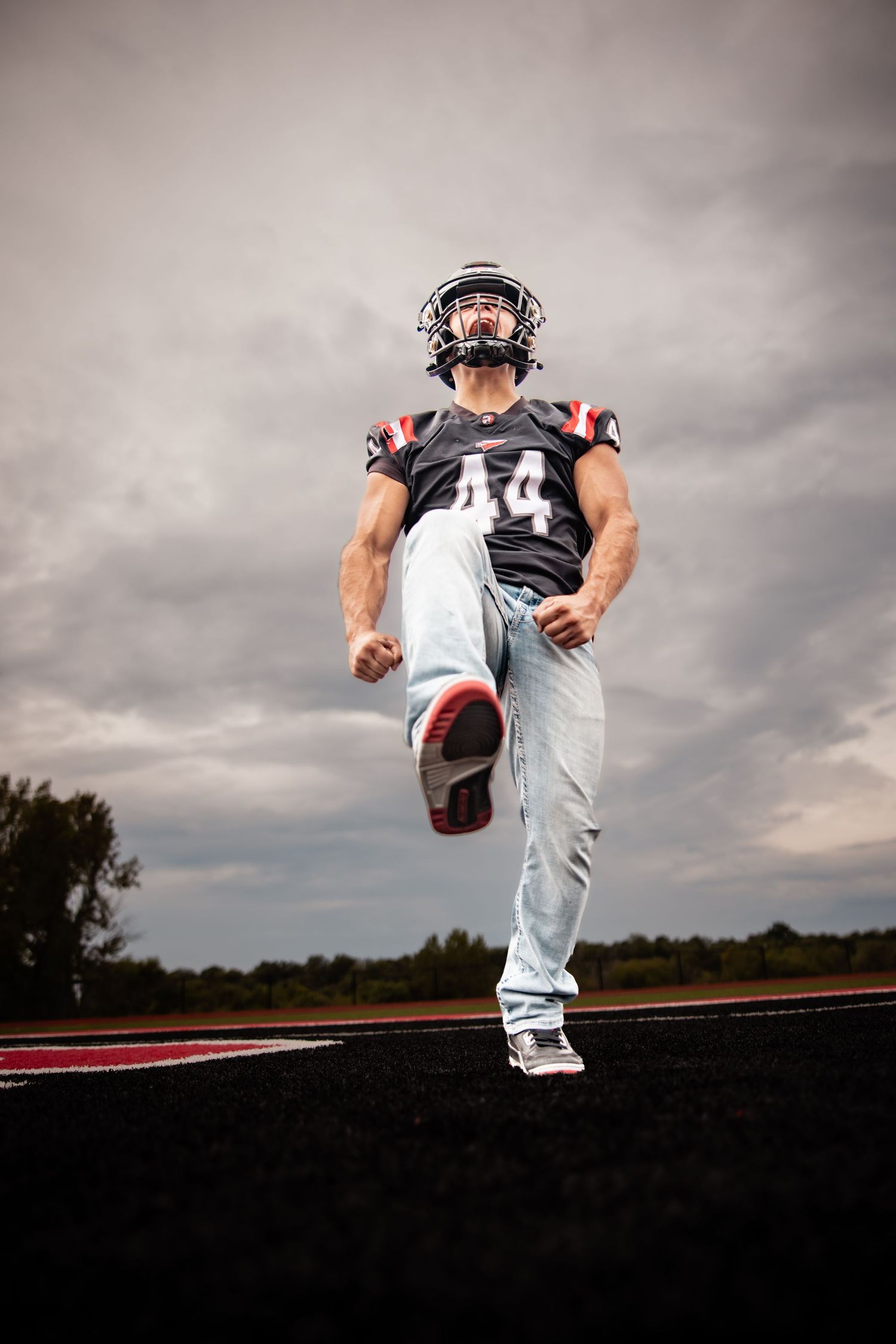 American football player #44 in helmet and jersey celebrates energetically on field under dramatic cloudy sky.