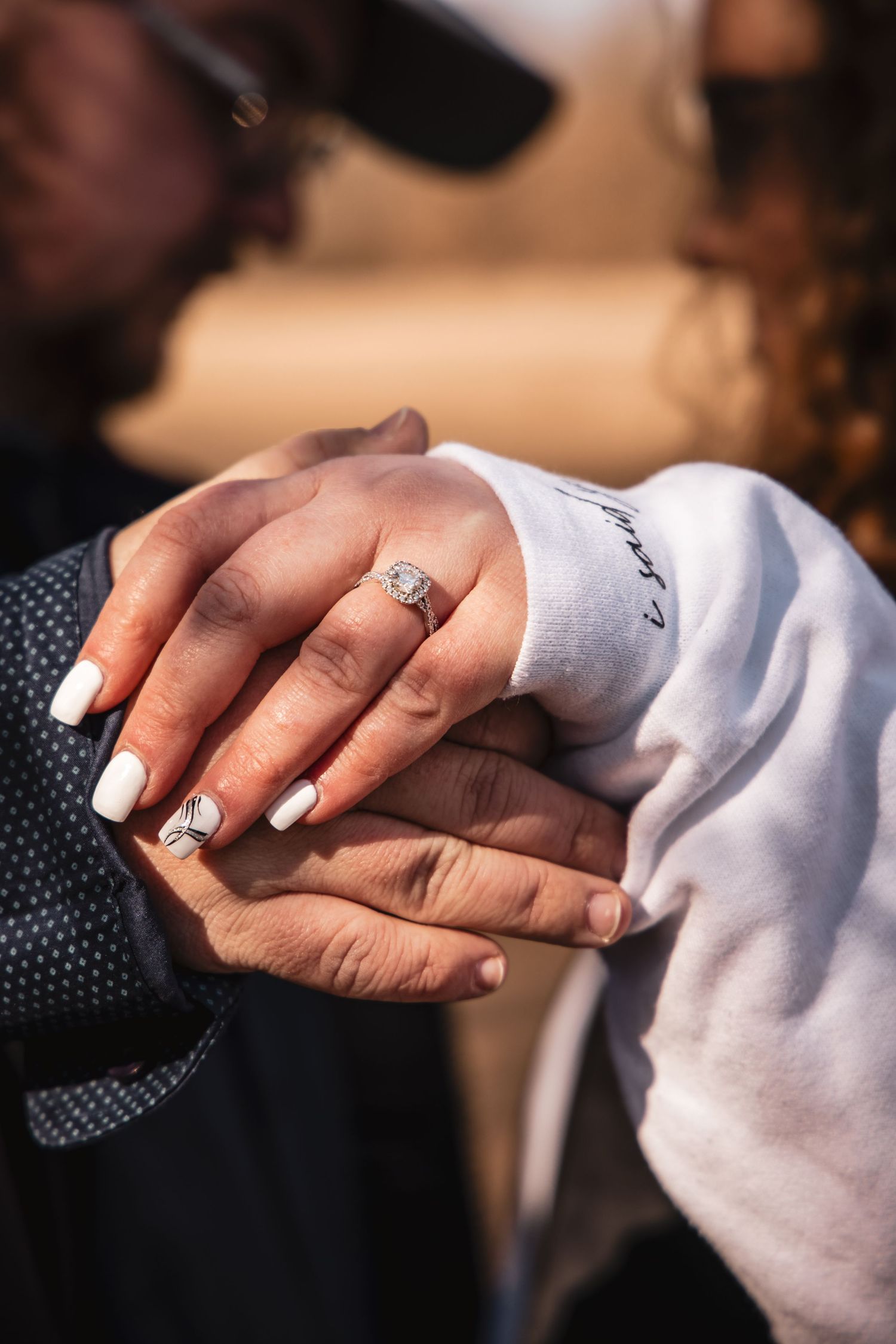 Close-up of couple holding hands displaying a diamond engagement ring with white manicured nails.