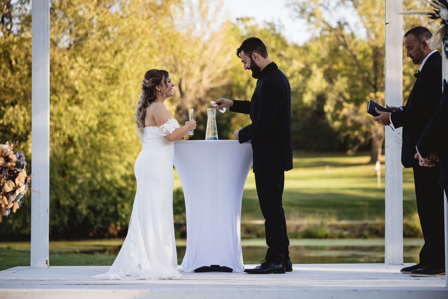 Bride and groom perform a unity ceremony at a white gazebo during their outdoor wedding.