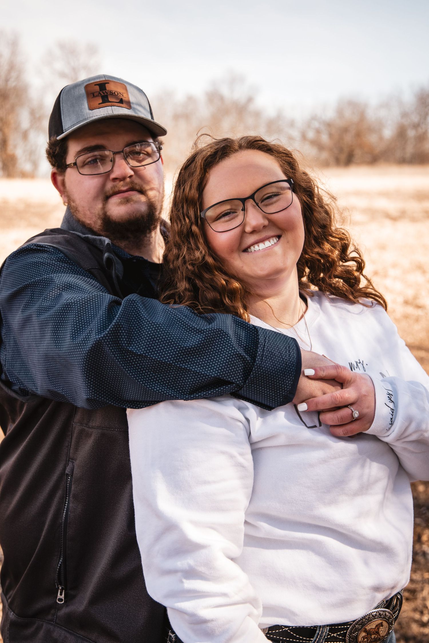 Happy couple embraces outdoors, woman with curly red hair smiling brightly in natural light.