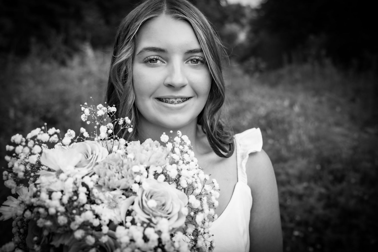 Black and white portrait of a smiling girl holding a bouquet of wildflowers and roses outdoors.
