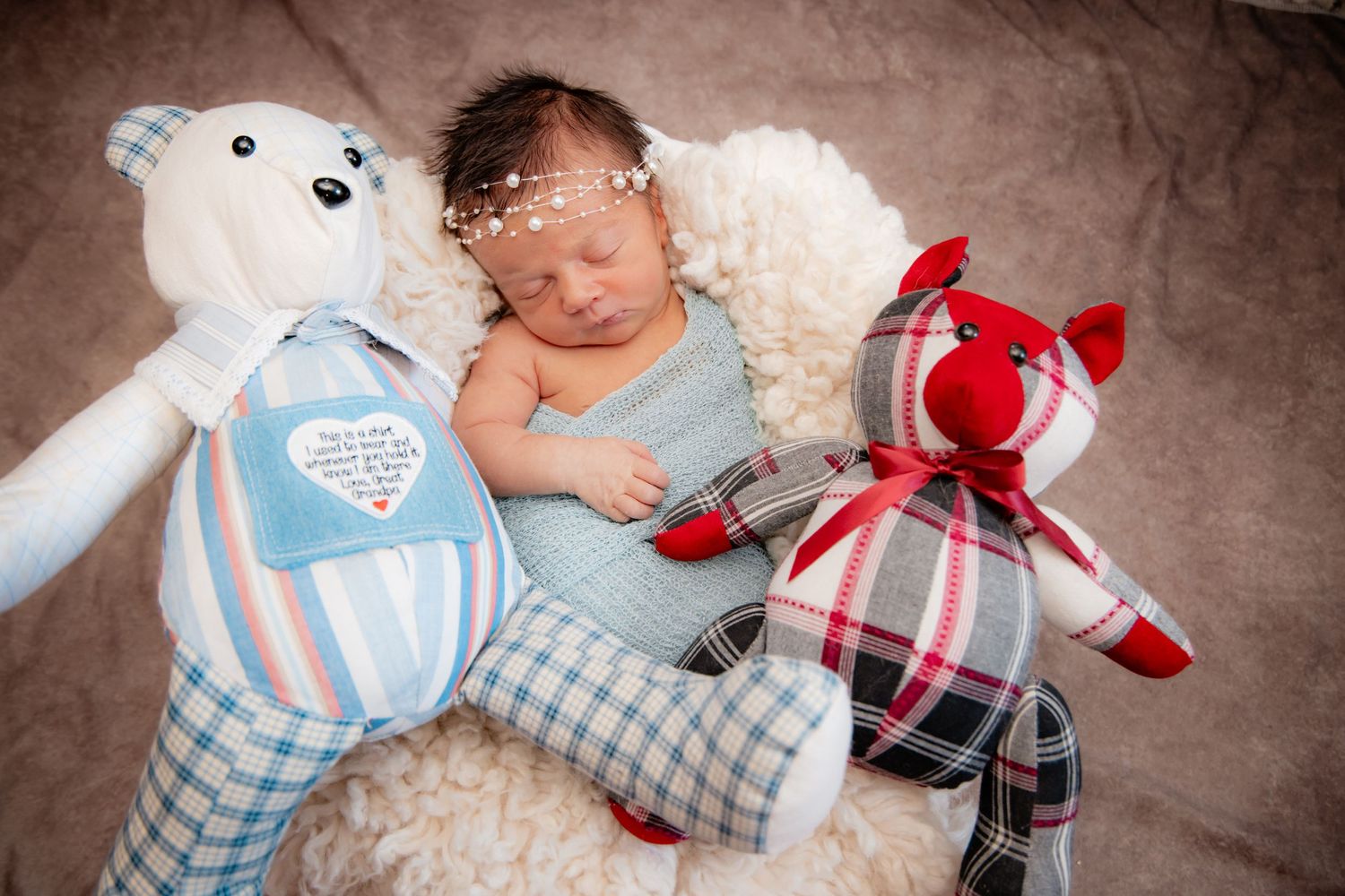 Newborn baby sleeping peacefully between two handmade plaid stuffed animals, a bear and fox, in a cozy nursery setting.