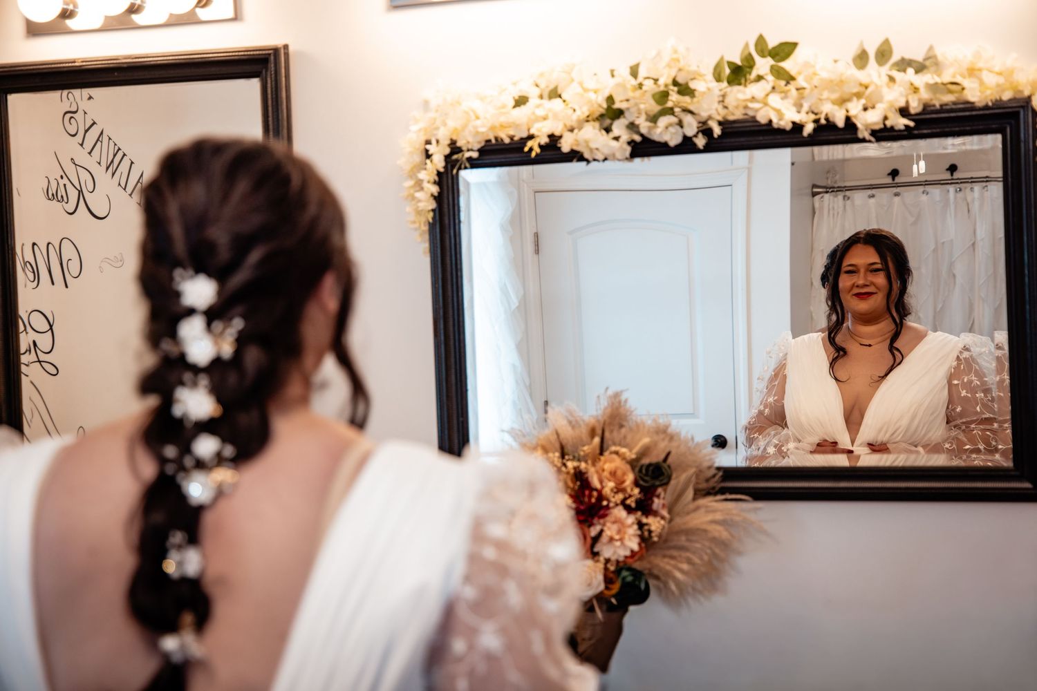 Bride with floral braided hair admiring her reflection in a mirror wearing a white lace gown.