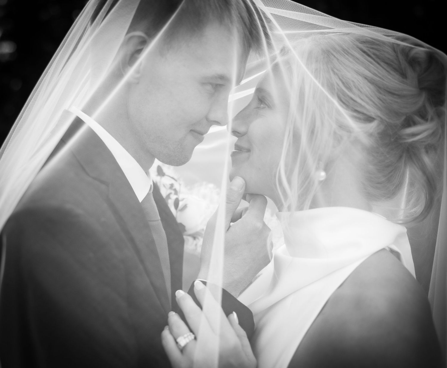 Black and white wedding photo of bride and groom sharing an intimate moment under a veil.