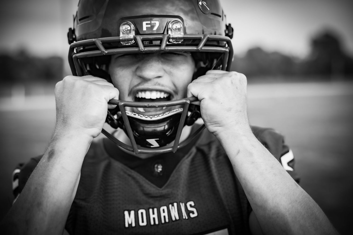 Intense Mohawks football player in helmet and pads grimacing aggressively, black and white action portrait.