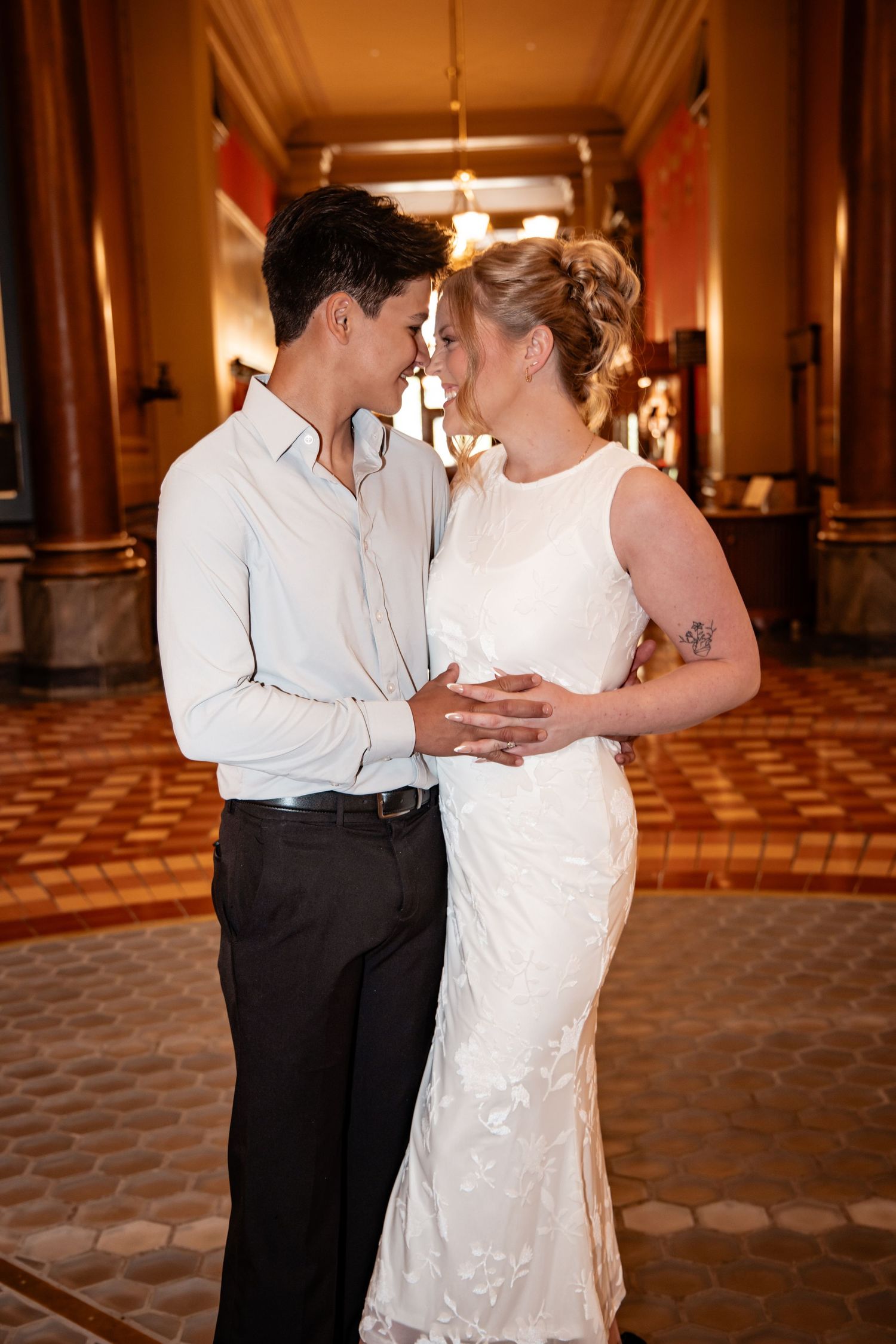 A bride and groom share a romantic moment in an elegant hall, touching foreheads tenderly.