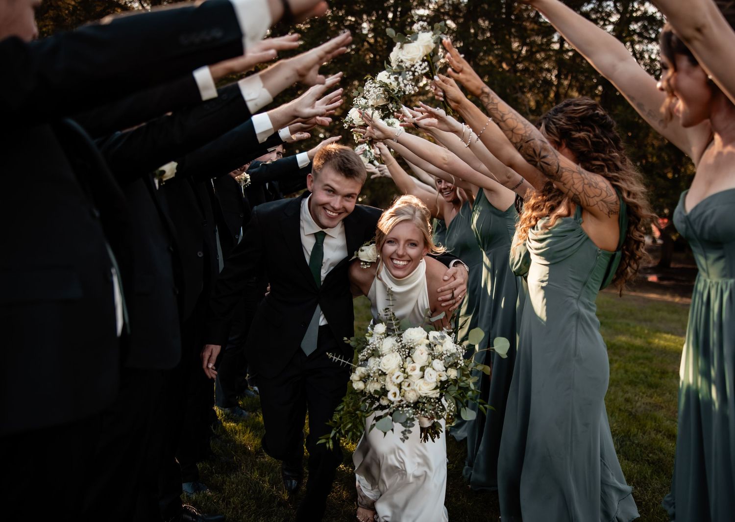 Bride and groom walk through an arch of raised hands formed by their wedding party.