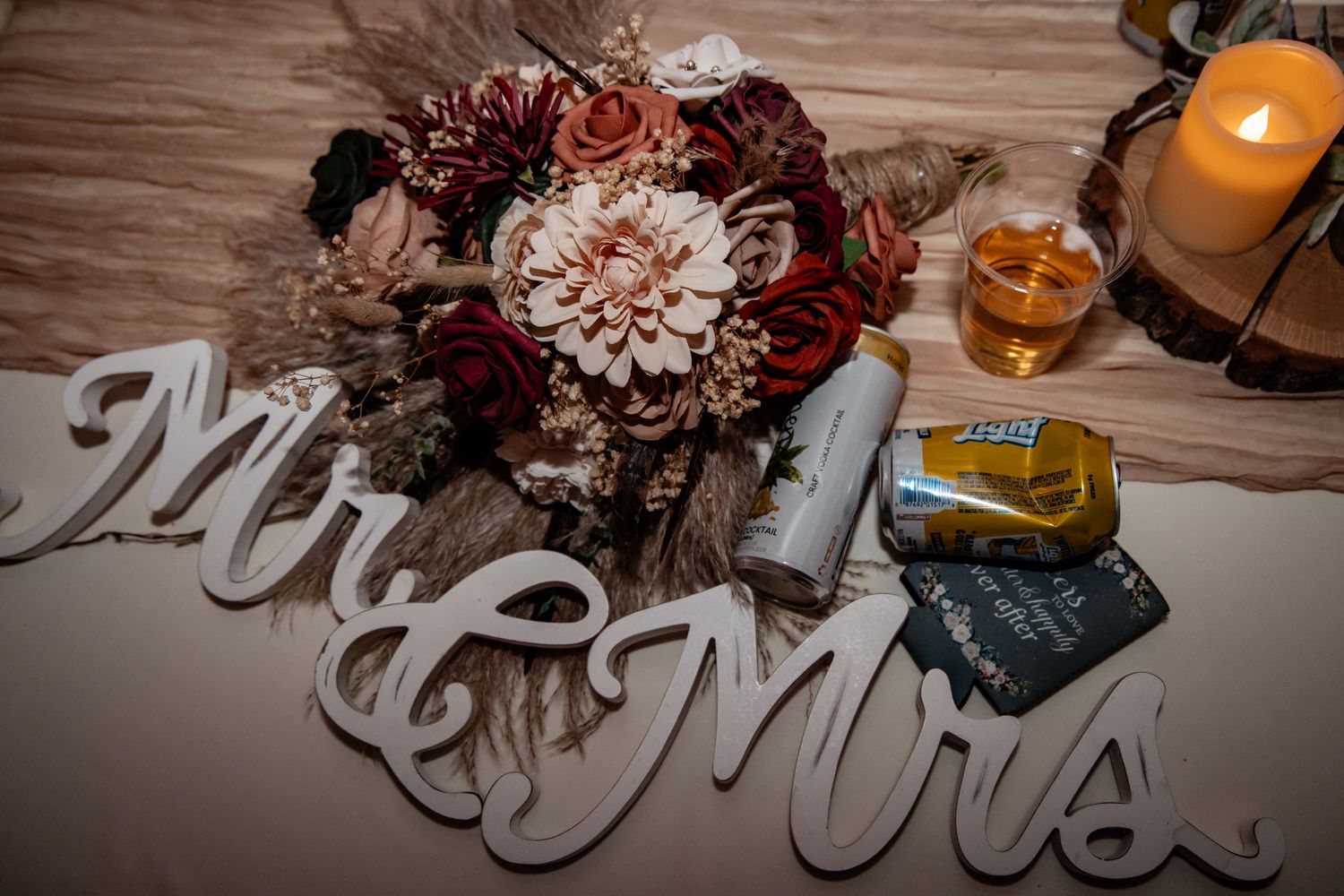 Mr and Mrs wooden sign with boho wedding bouquet featuring red and blush dahlias on a rustic table.