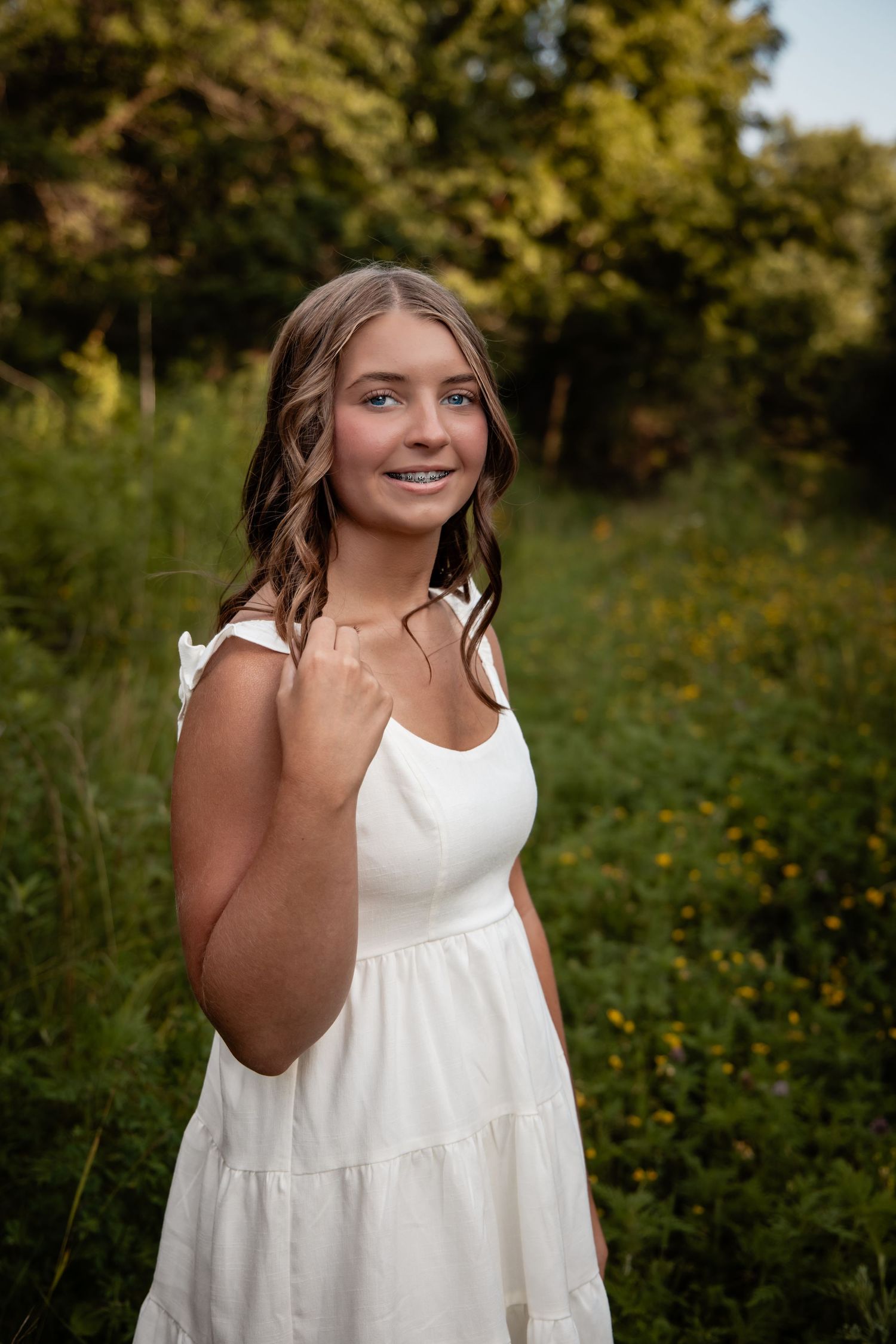 Young girl in white dress smiling outdoors in green field.