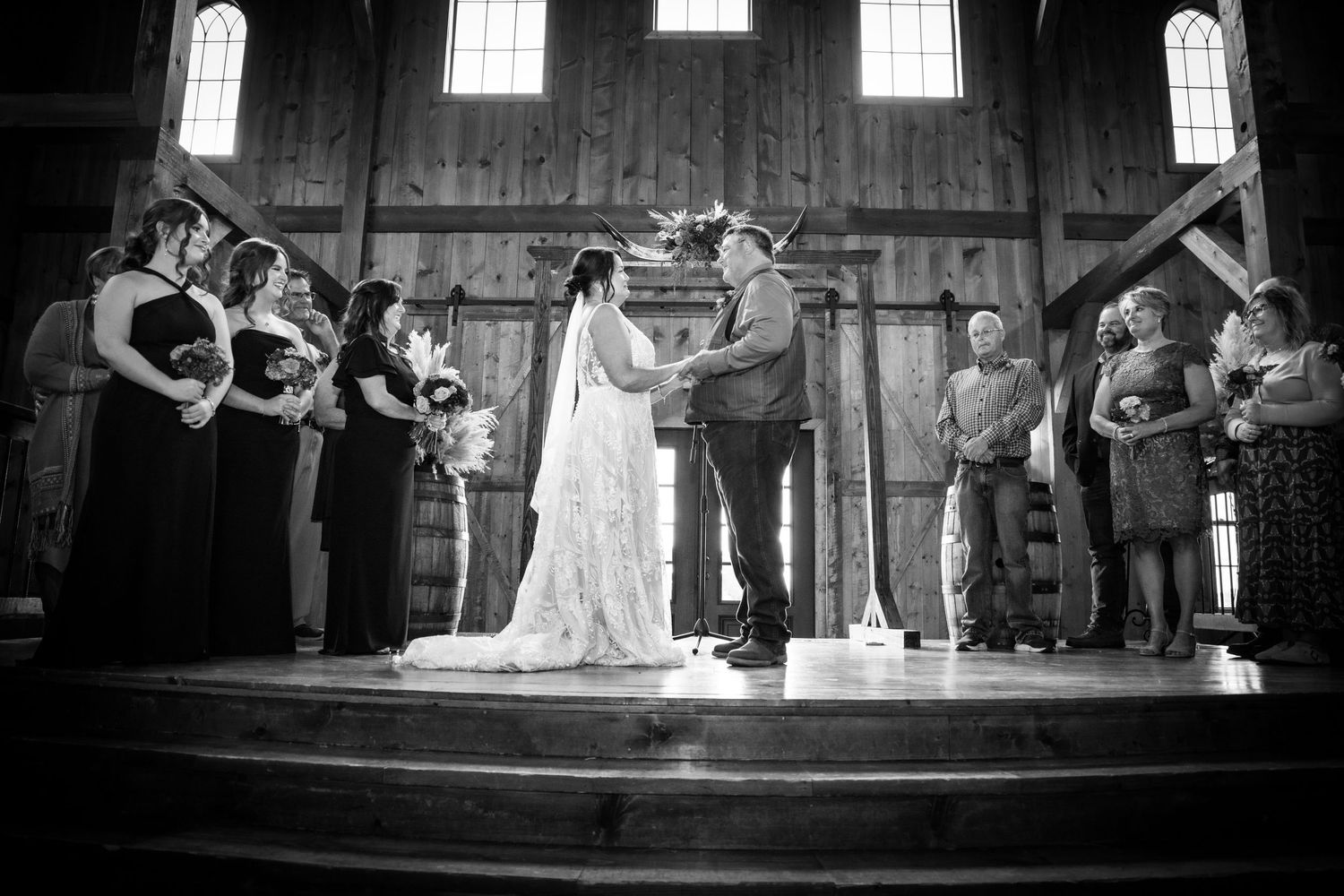 Black and white photo of bride and groom exchanging vows inside a rustic barn wedding.