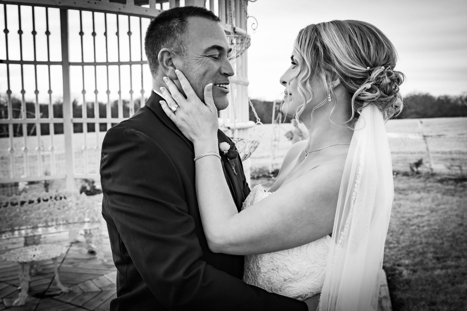 Black and white romantic portrait of bride tenderly holding grooms face during outdoor wedding photo session.