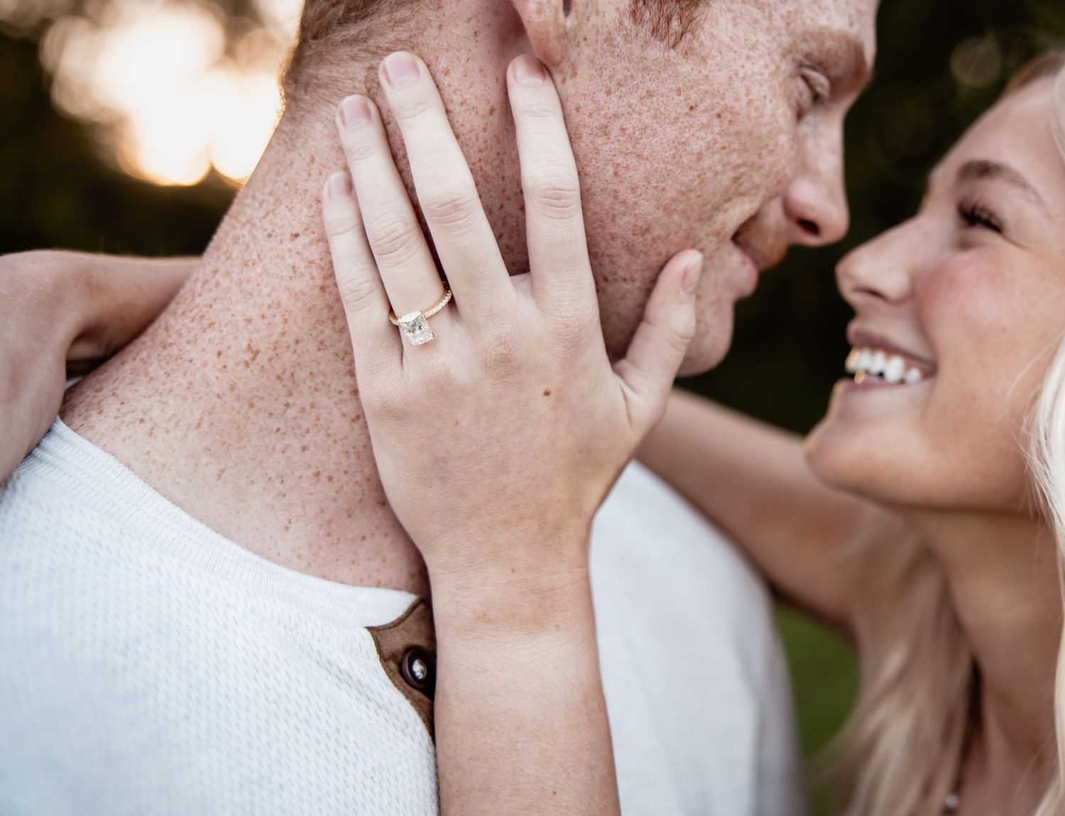 Couple sharing a romantic moment, woman displaying diamond engagement ring on her hand against man's cheek.