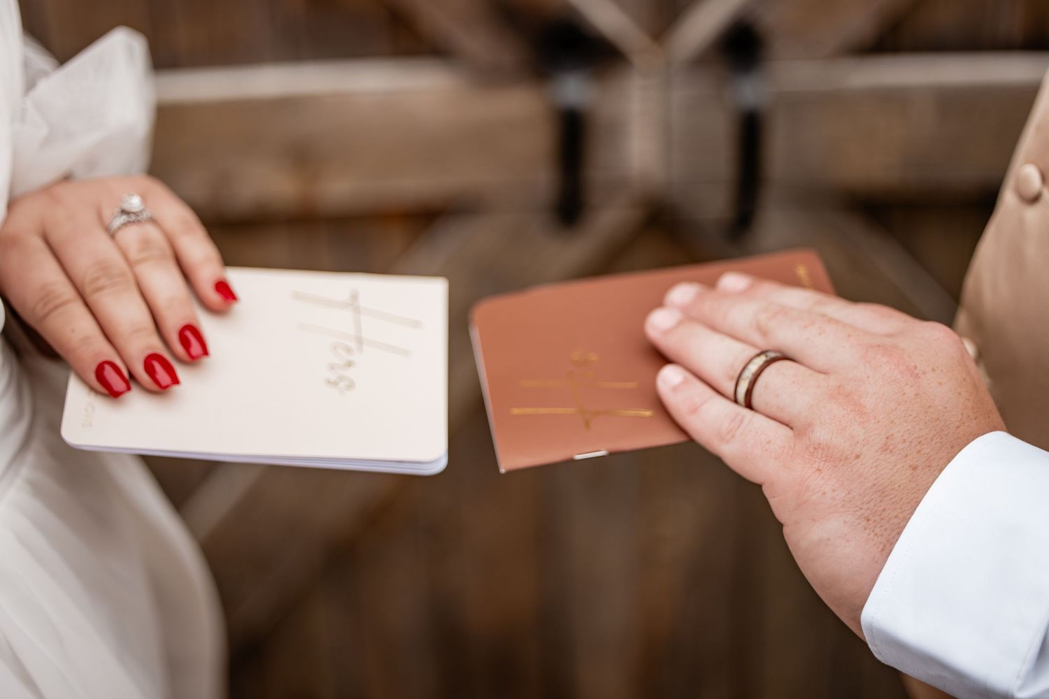 Close-up of bride and groom exchanging handwritten vow booklets during wedding ceremony.