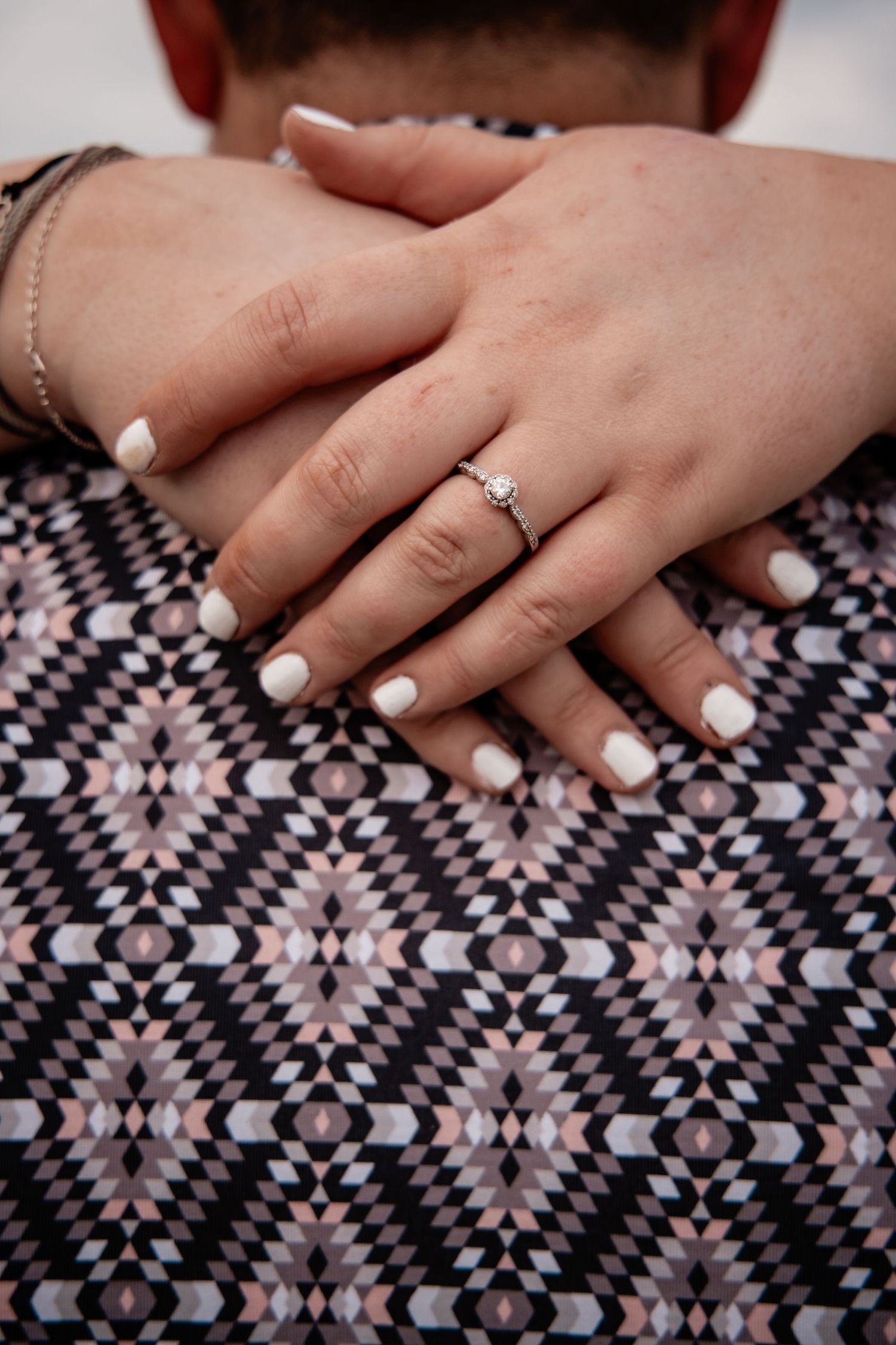 Close-up of engagement ring on bride's hand resting on partner's patterned shirt.