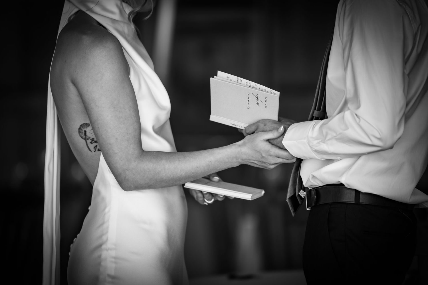 Bride and groom exchange vows holding hands during wedding ceremony in black and white photo.