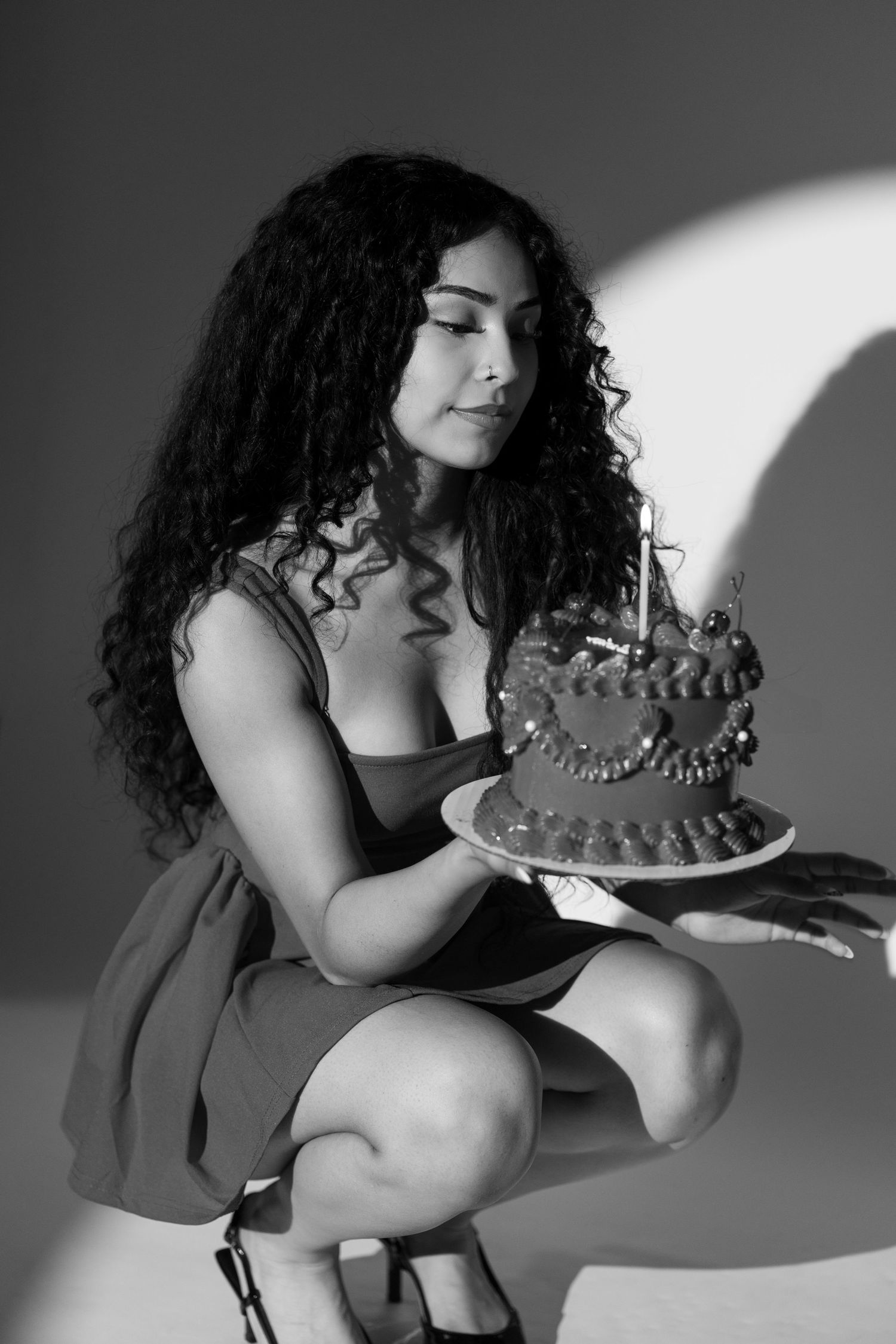 Black and white photo of woman in dress holding birthday cake with candle.