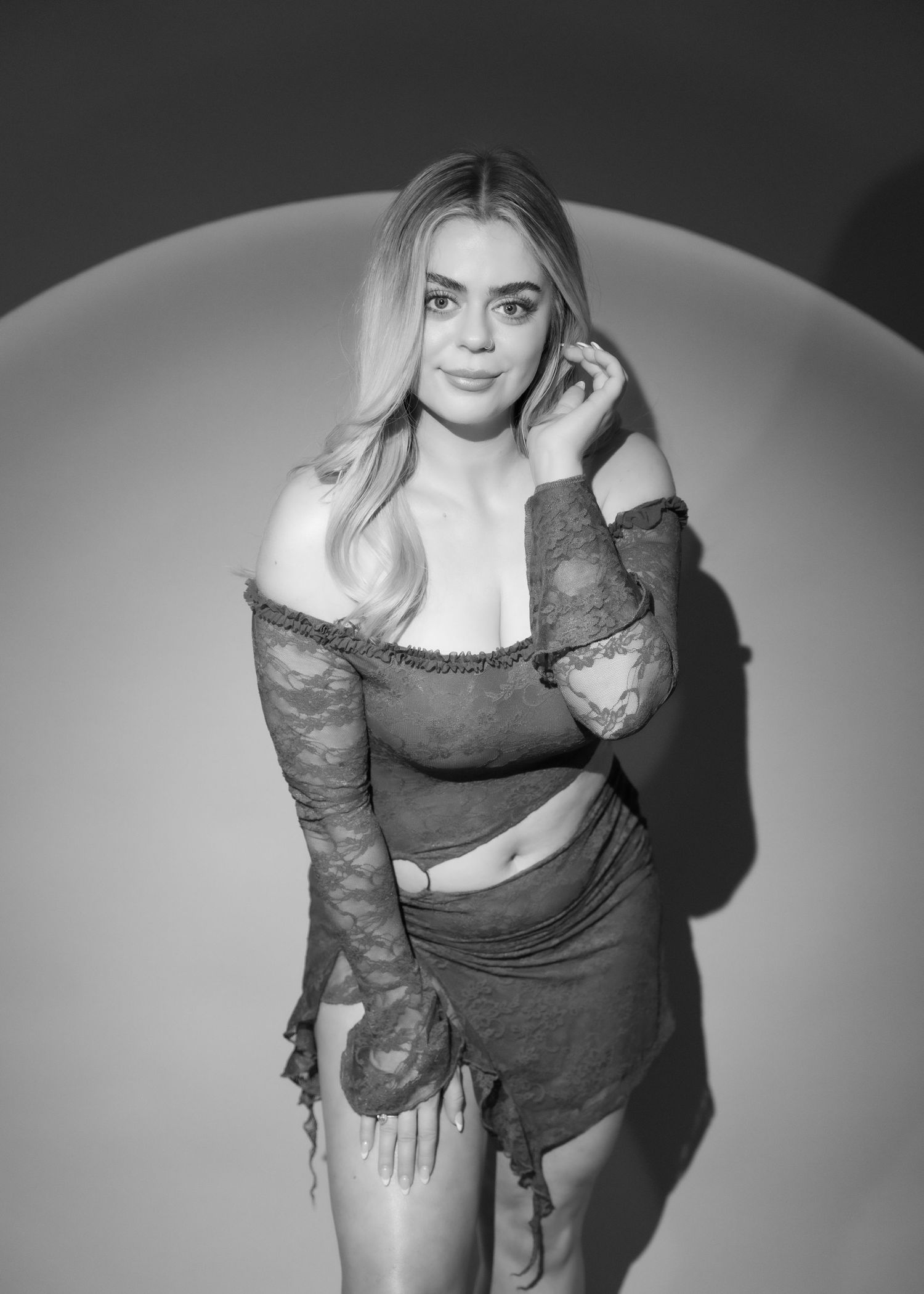 Black and white portrait of blonde woman in lace off-shoulder two-piece outfit in studio setting.