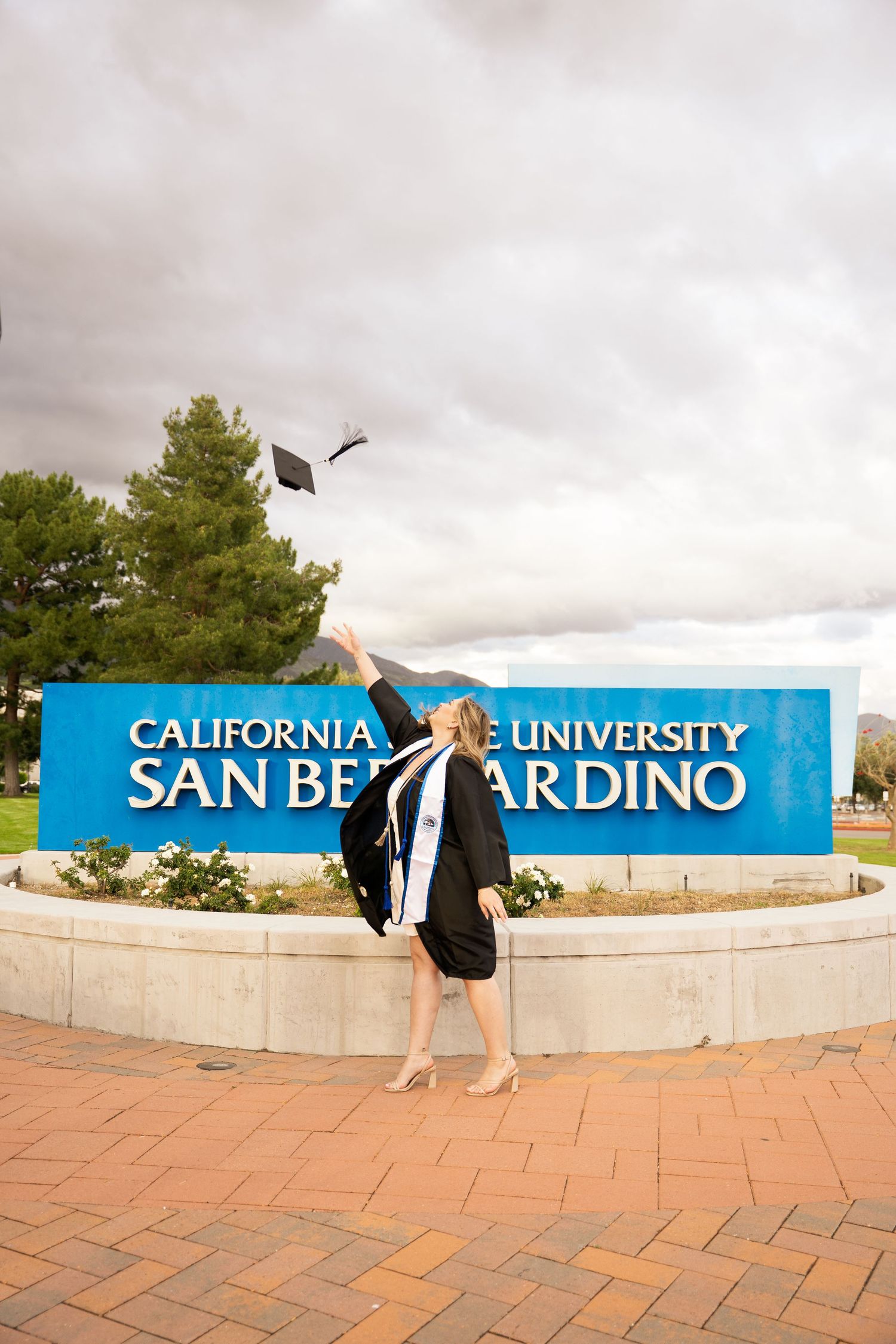 Graduate tosses cap in air in front of California State University San Bernardino sign.