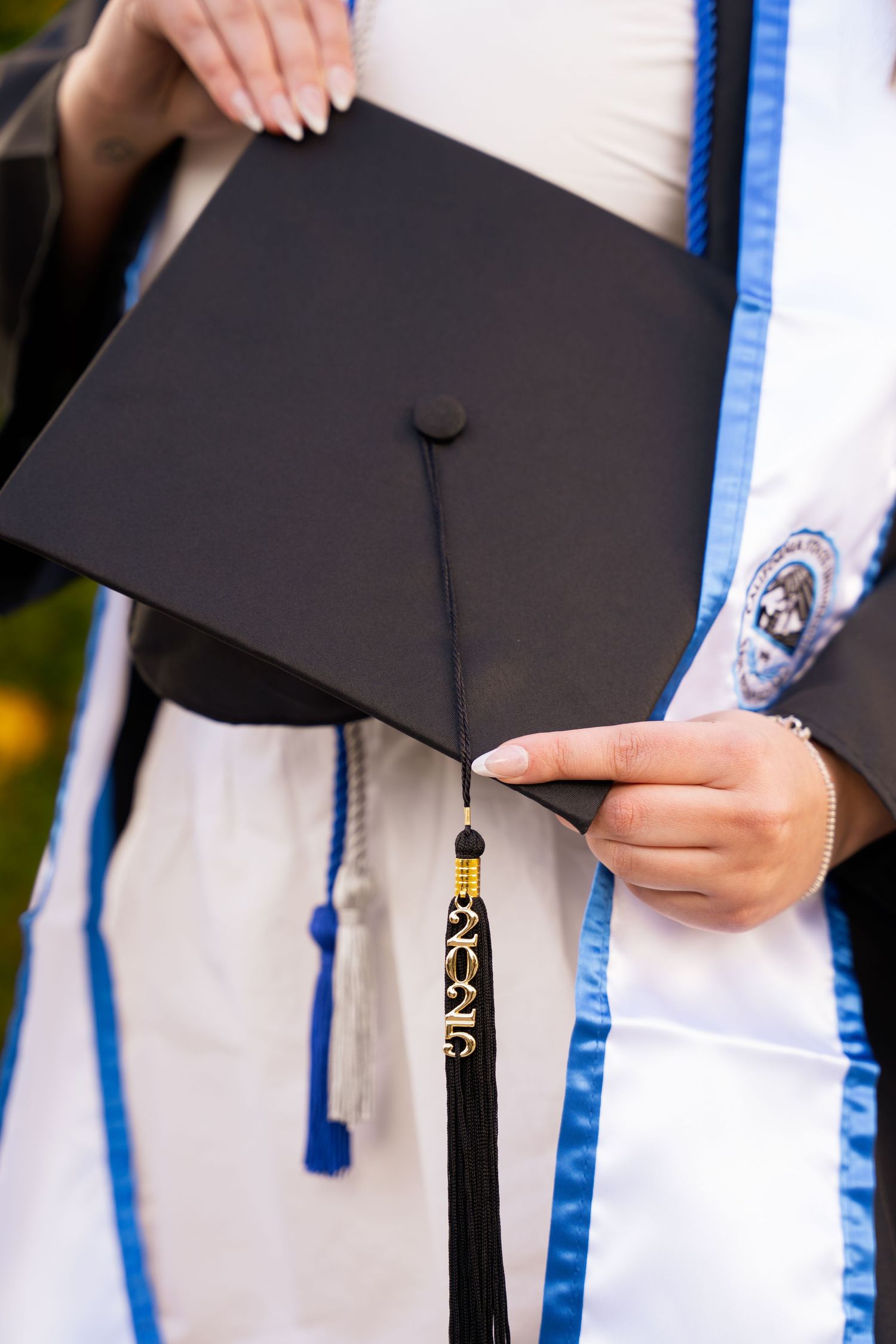 Close-up of a graduate holding a black mortarboard cap with gold tassel in academic regalia.