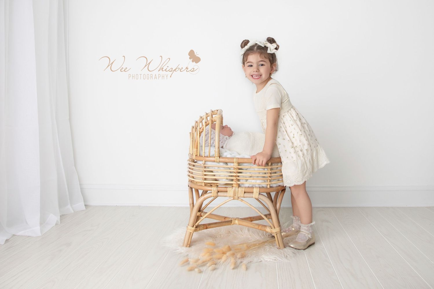 Little girl standing beside baby in cradle during infant photography session