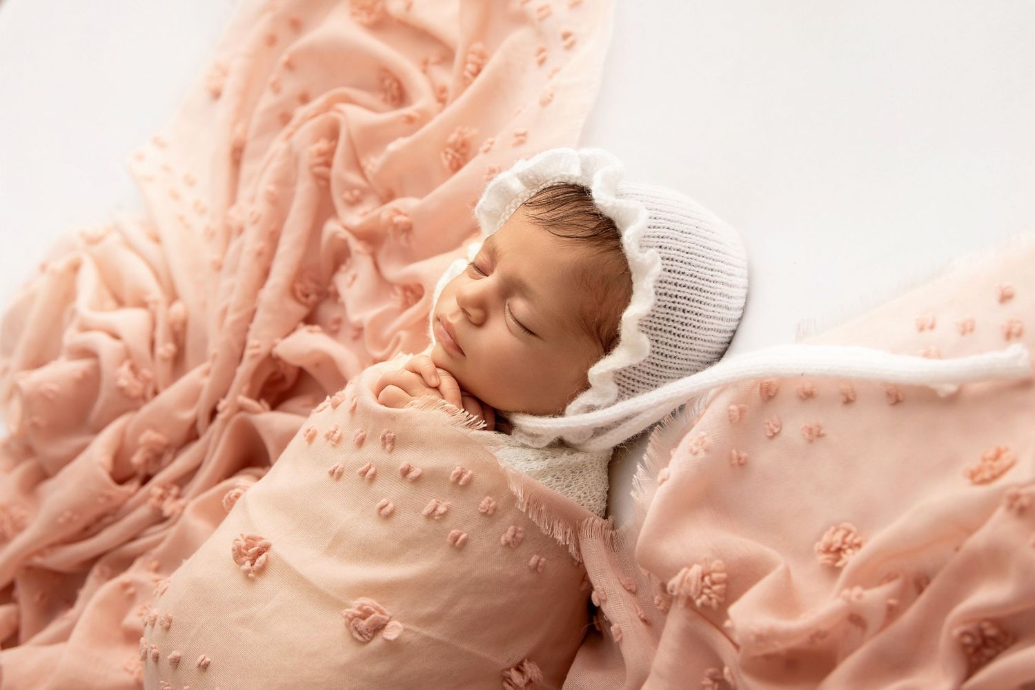 Sleeping newborn baby wrapped in soft pink blanket with bonnet Baby resting on pink textured blanket wearing knit cap in studio portrait.