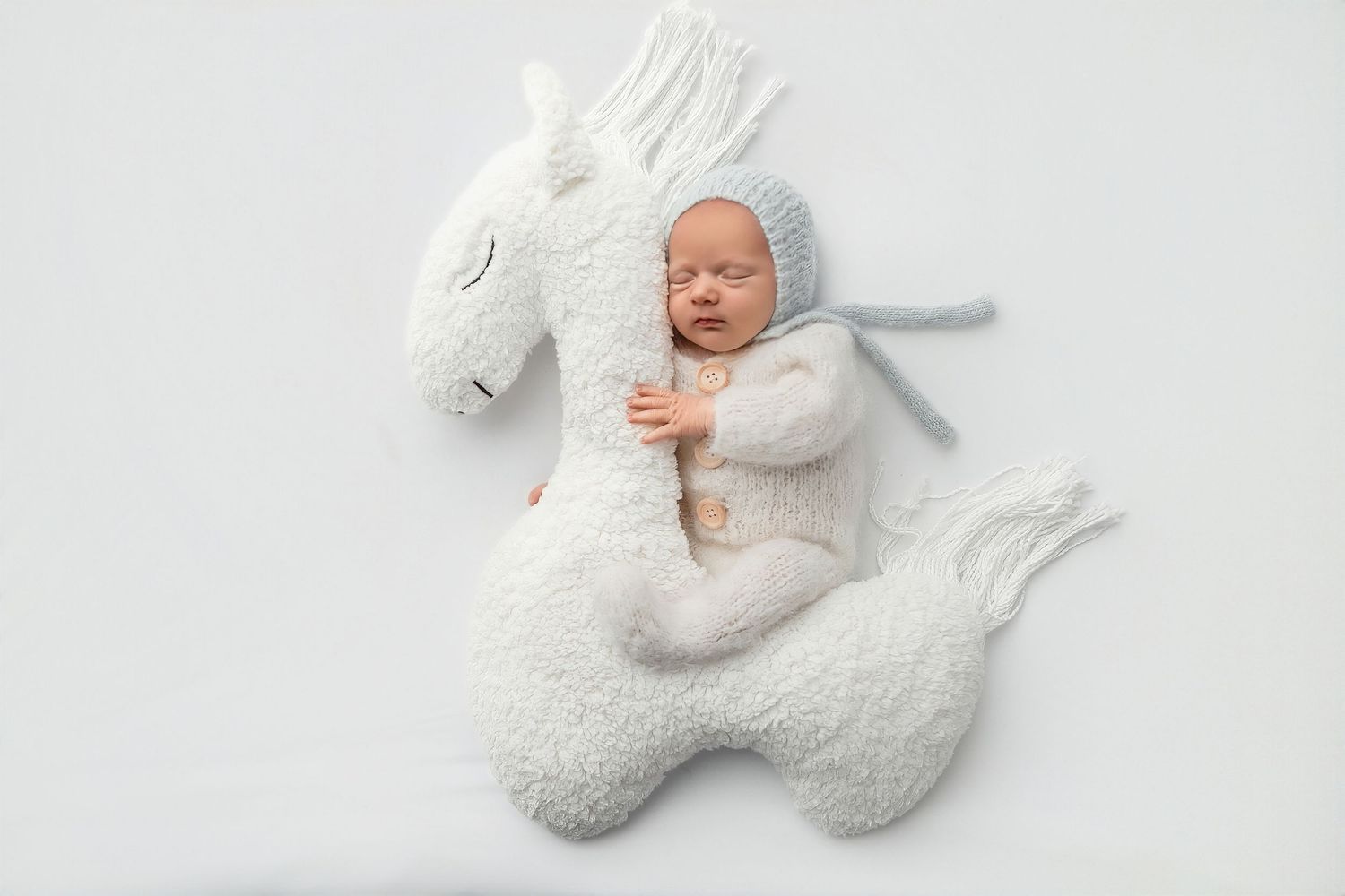 Peaceful sleeping baby in soft neutral outfit cuddling a plush toy during a professional newborn photoshoot in a calm studio setting