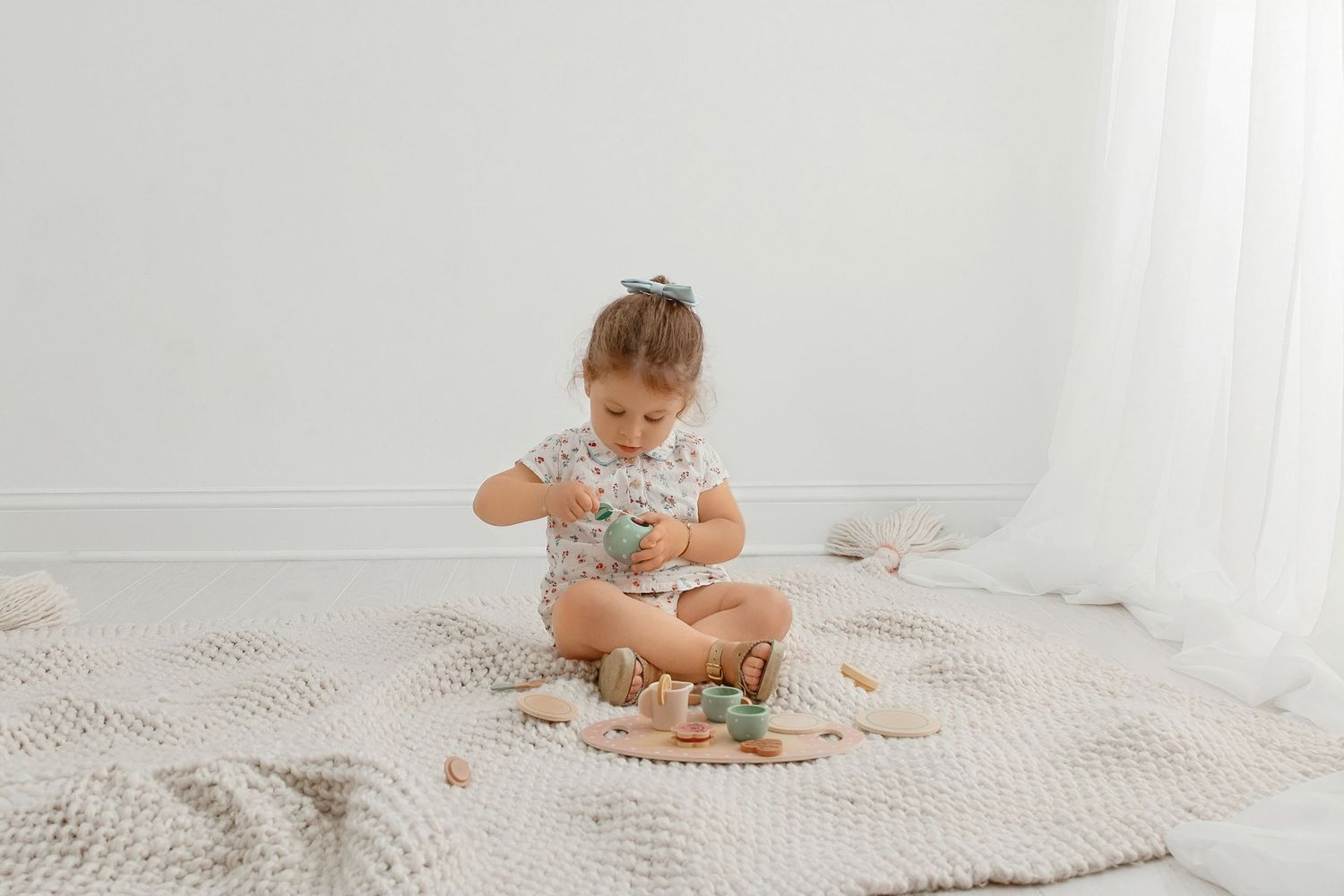 Milestone photography of baby girl sitting and playing with toys in soft neutral setup for infant photography session