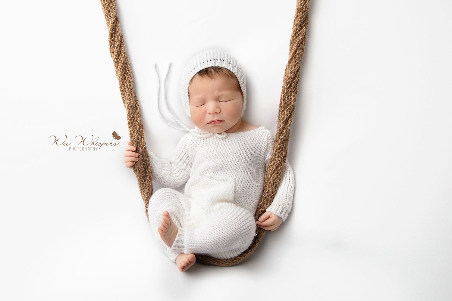 Sleeping baby in knit outfit resting in a swing during newborn photography session