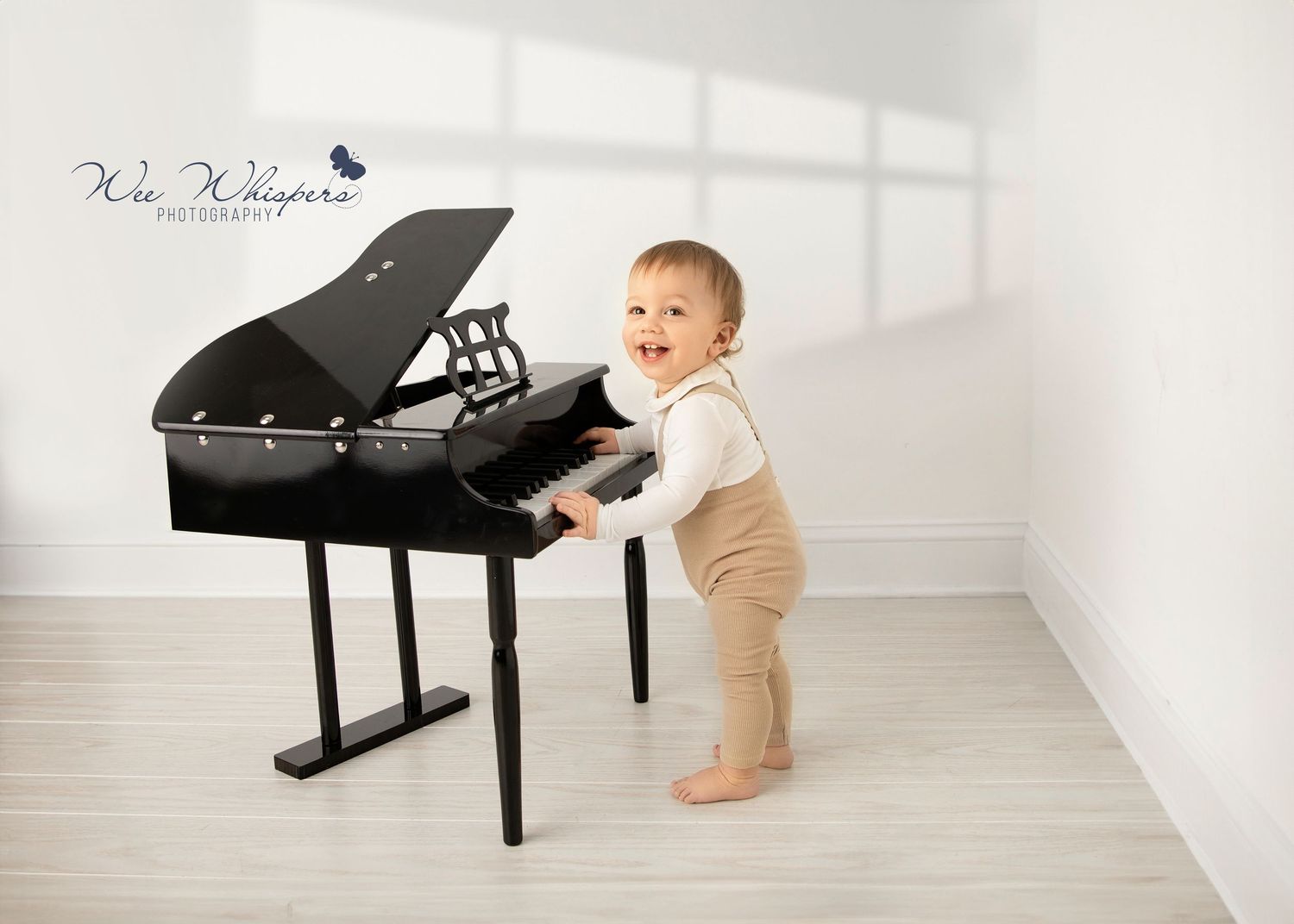 Baby exploring black piano in minimalist white studio setting.