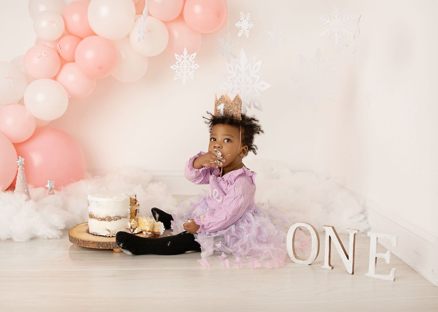 First birthday photoshoot with baby in dress enjoying cake during milestone photography session