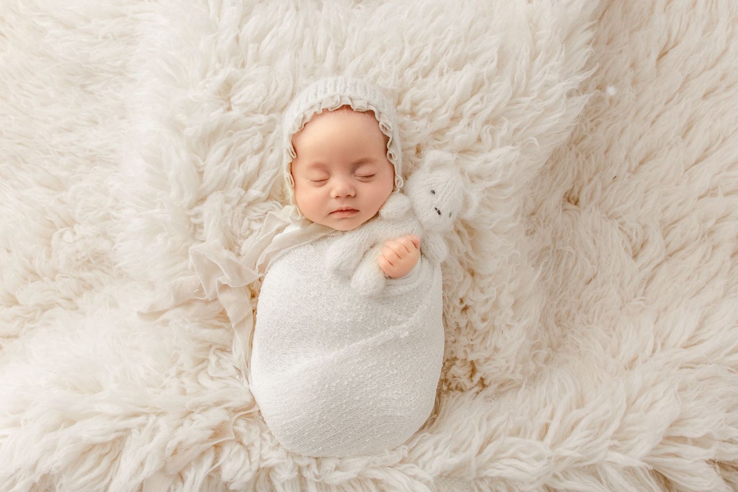 Newborn photoshoot with swaddled baby holding soft toy on textured blanket