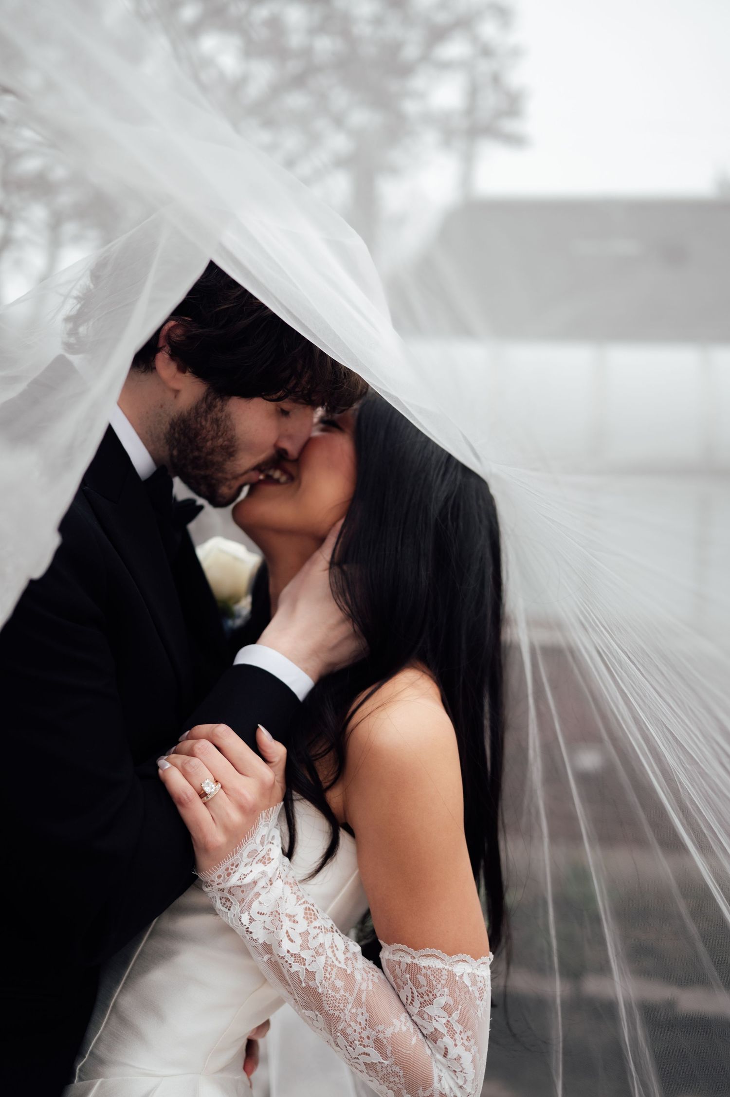 Bride and groom sharing a romantic kiss under a flowing white veil on their wedding day.