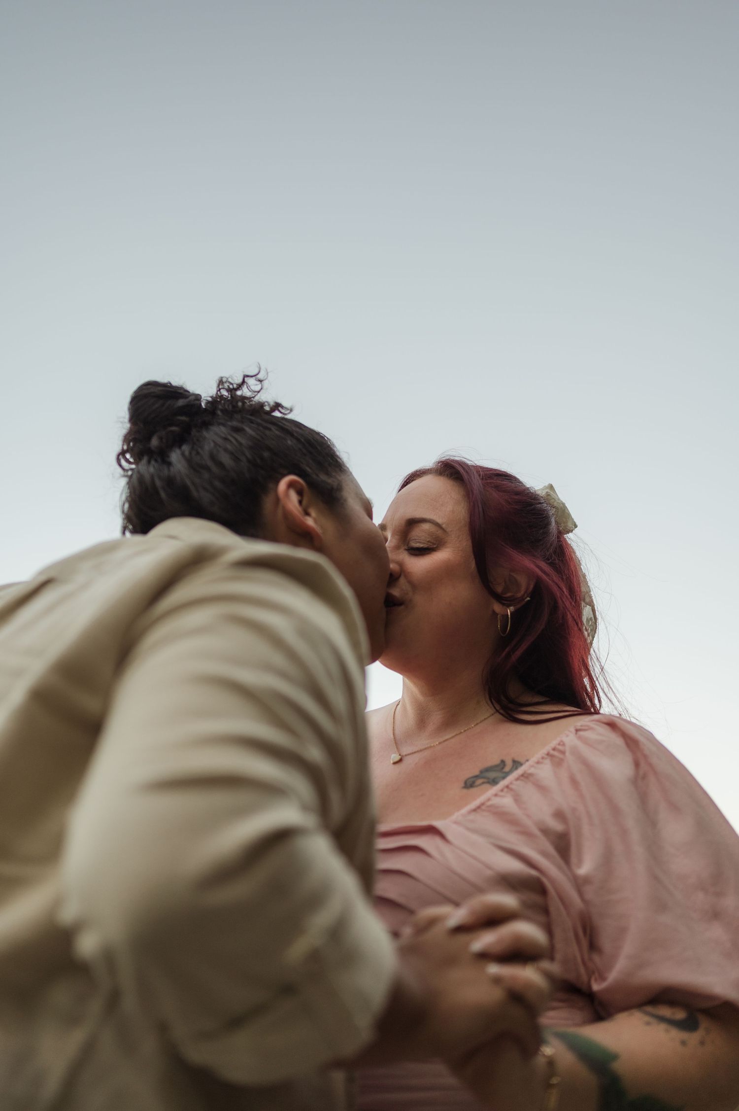 A couple in casual clothing sharing an intimate moment against an overcast sky.