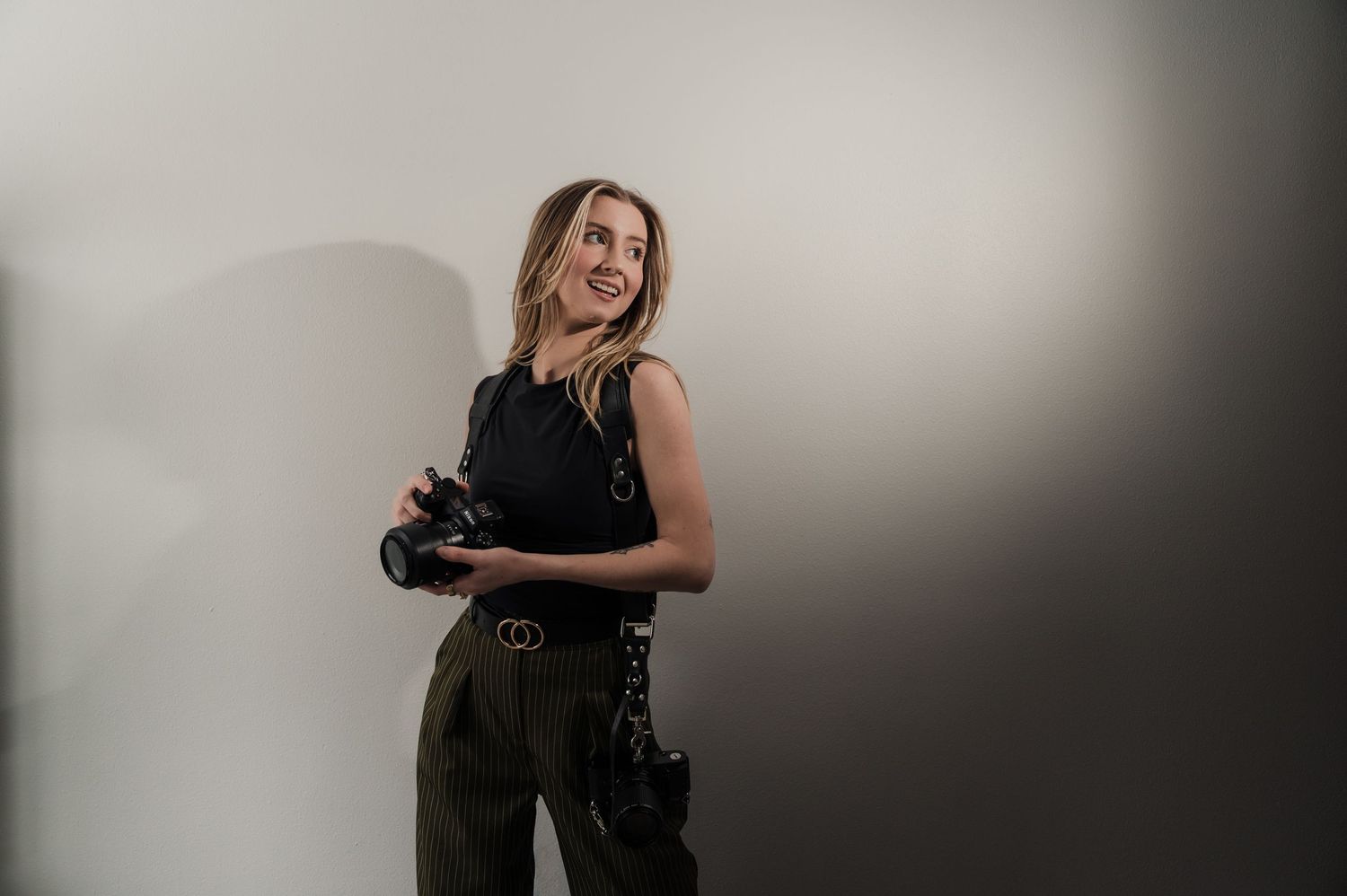 Professional photographer in black dress holding camera and posing in studio setting.