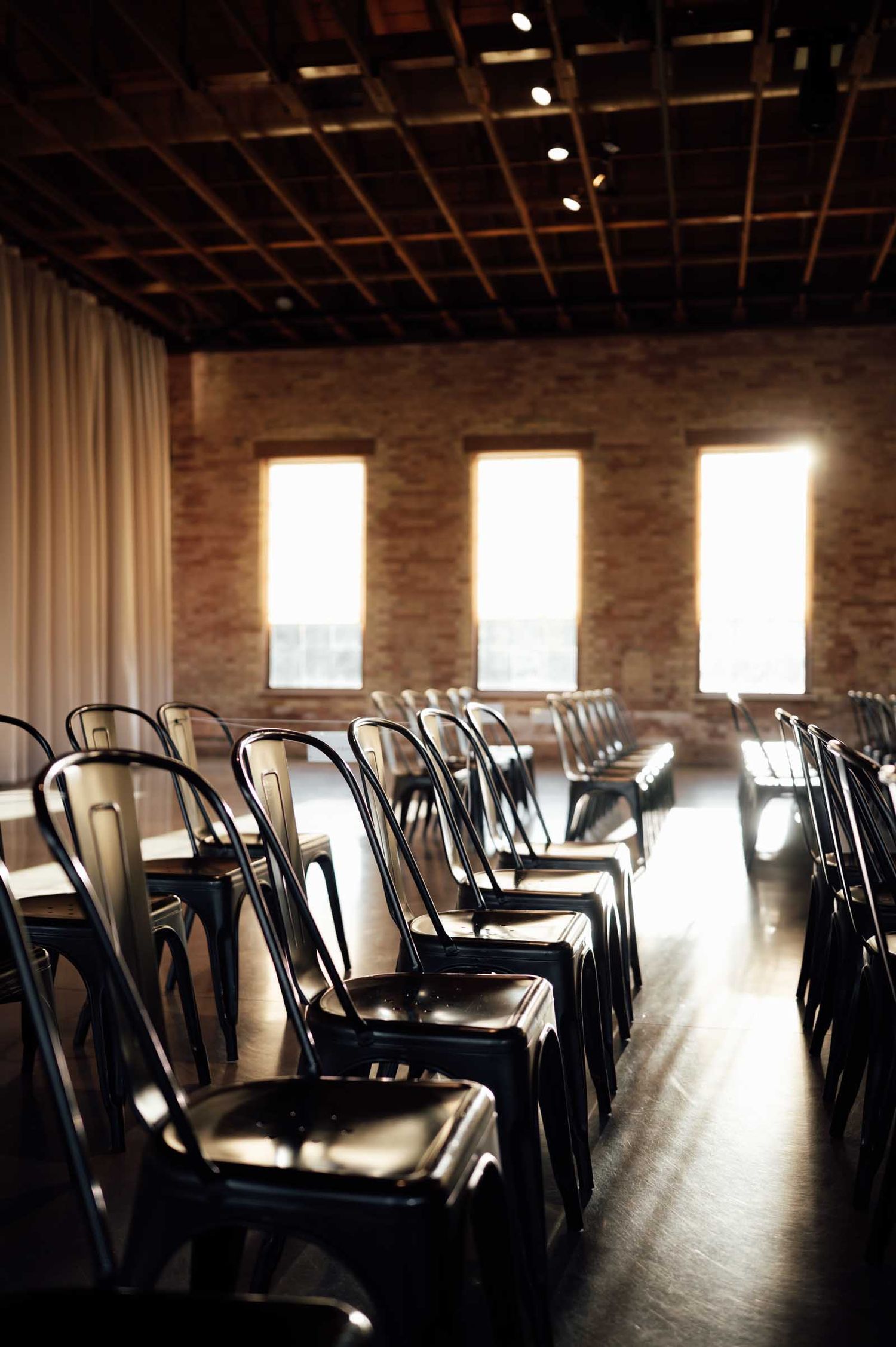 Rows of metal bistro chairs arranged in an industrial venue with brick walls, wooden ceiling, and bright windows.