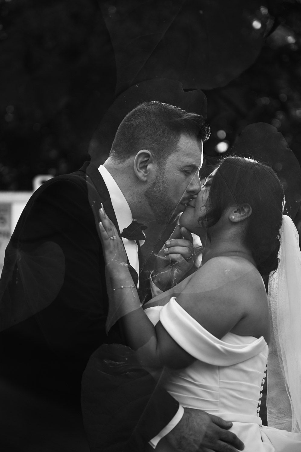 Black and white photo of bride and groom sharing a romantic first kiss at their wedding ceremony.