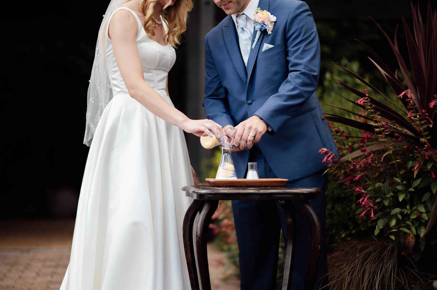 Bride and groom performing a unity sand ceremony at their wedding reception outdoors.