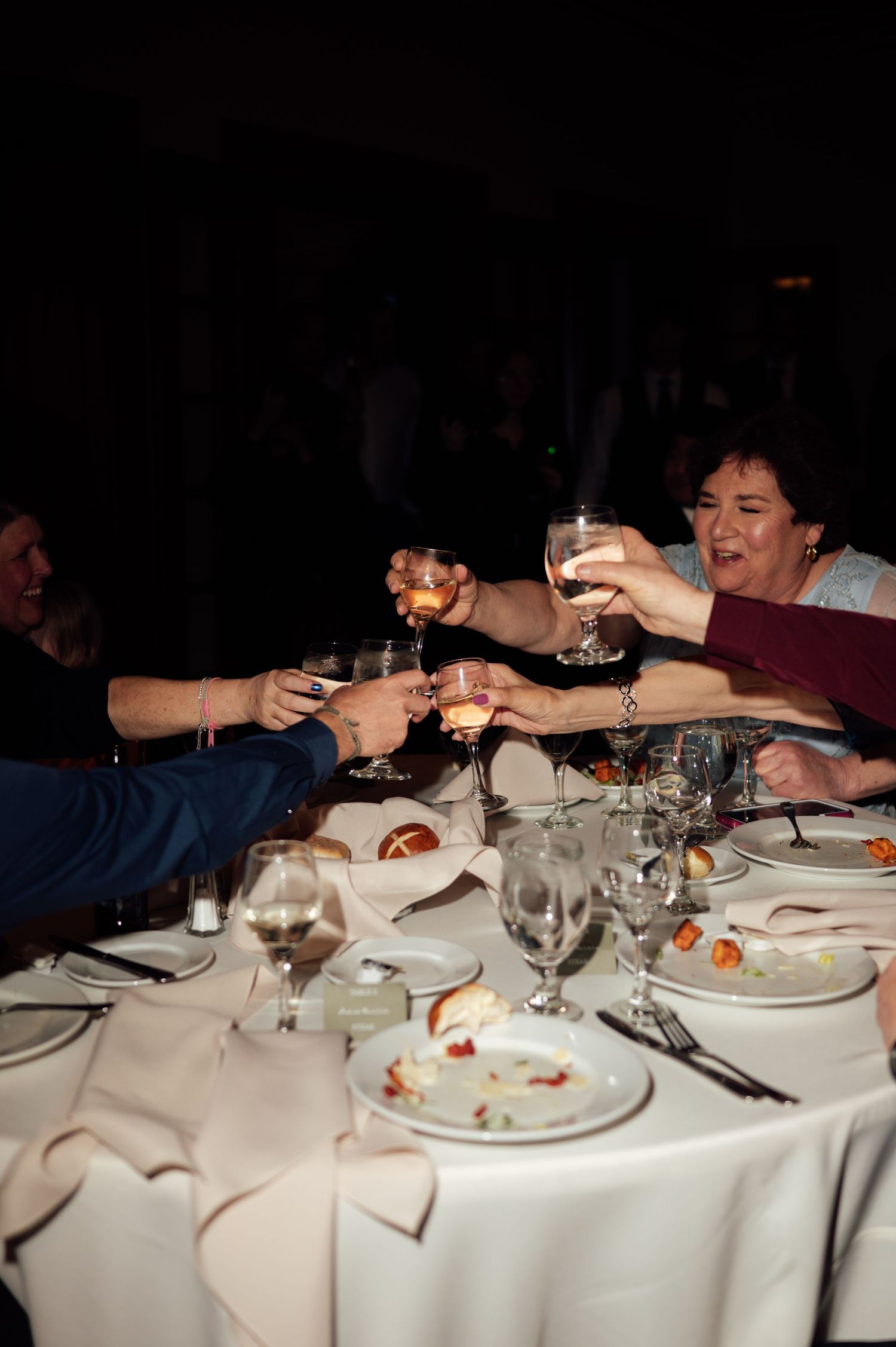 Group of people raising wine glasses in a toast at a formal dinner table with white tablecloth and elegant place settings.