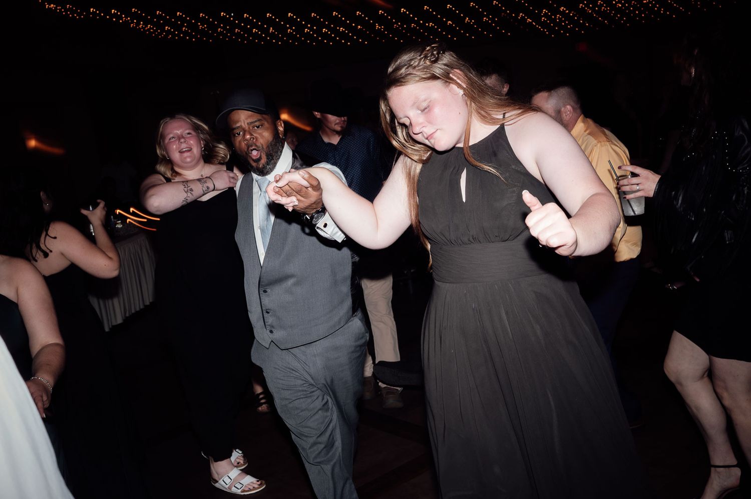 Couple dancing together at a formal event, man in gray suit and woman in black gown, at a lively party.