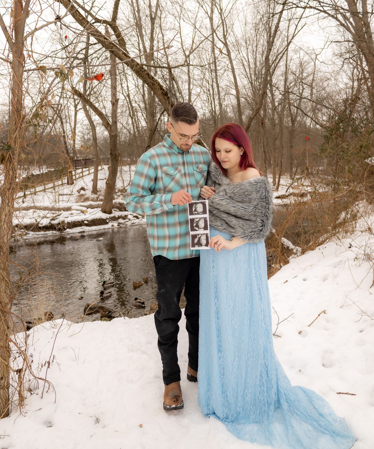 Winter engagement photo session with a flowing light blue dress against snowy landscape.
