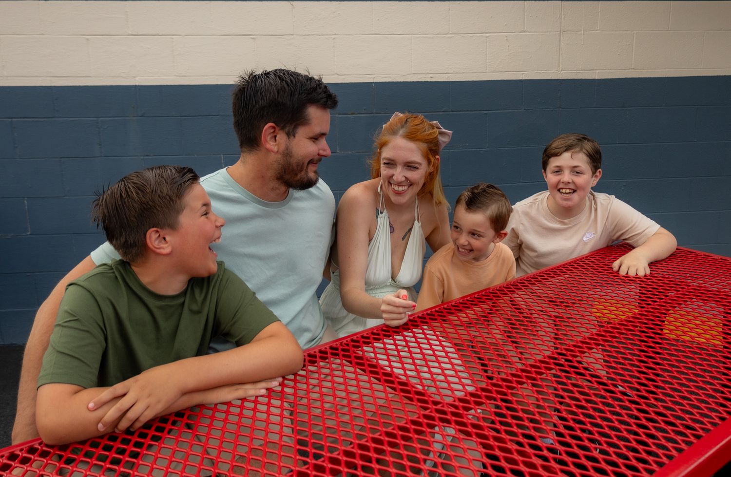 A group plays a tabletop game with a red net and white balls while laughing and having fun together.