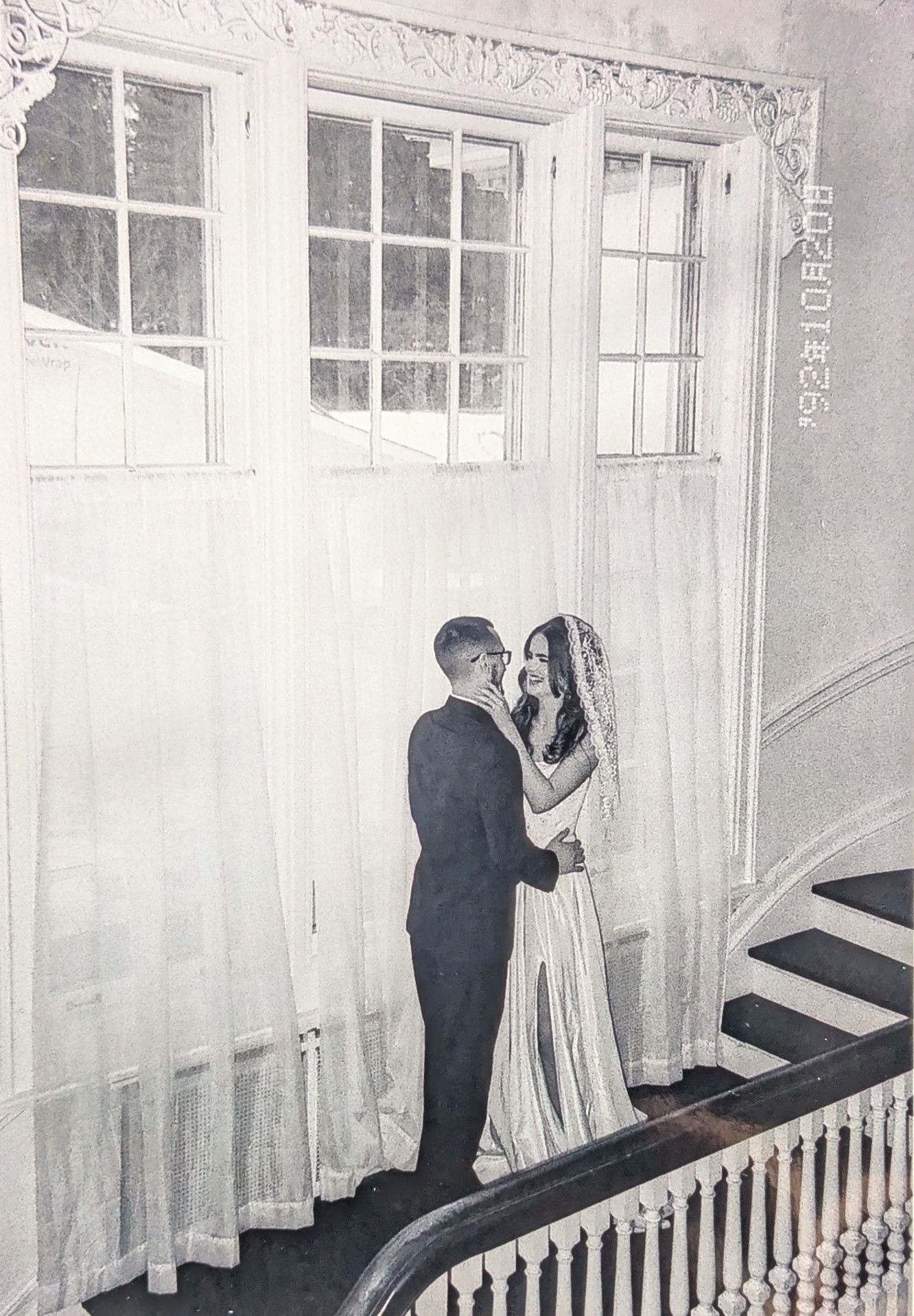 A romantic black and white photograph of a couple sharing an intimate moment on a staircase with white curtains.