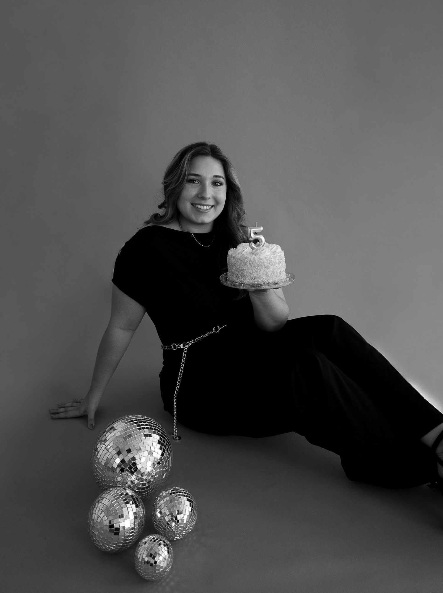 A black and white artistic photo series showing someone in a black outfit posing with disco balls on a light background.