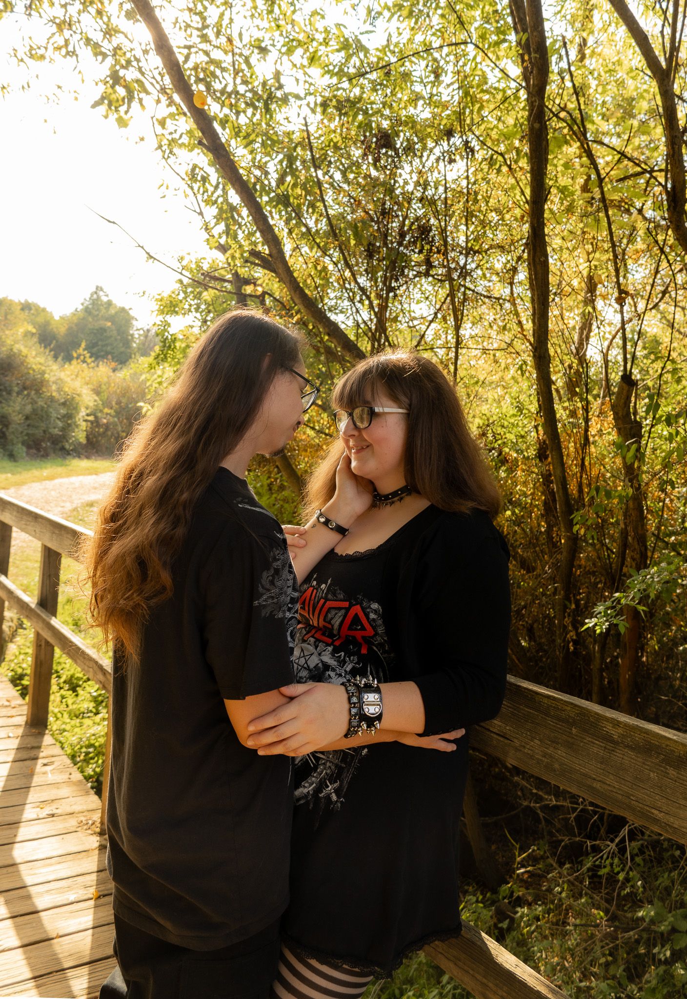 Romantic photoshoot on wooden boardwalk during golden hour with natural foliage.