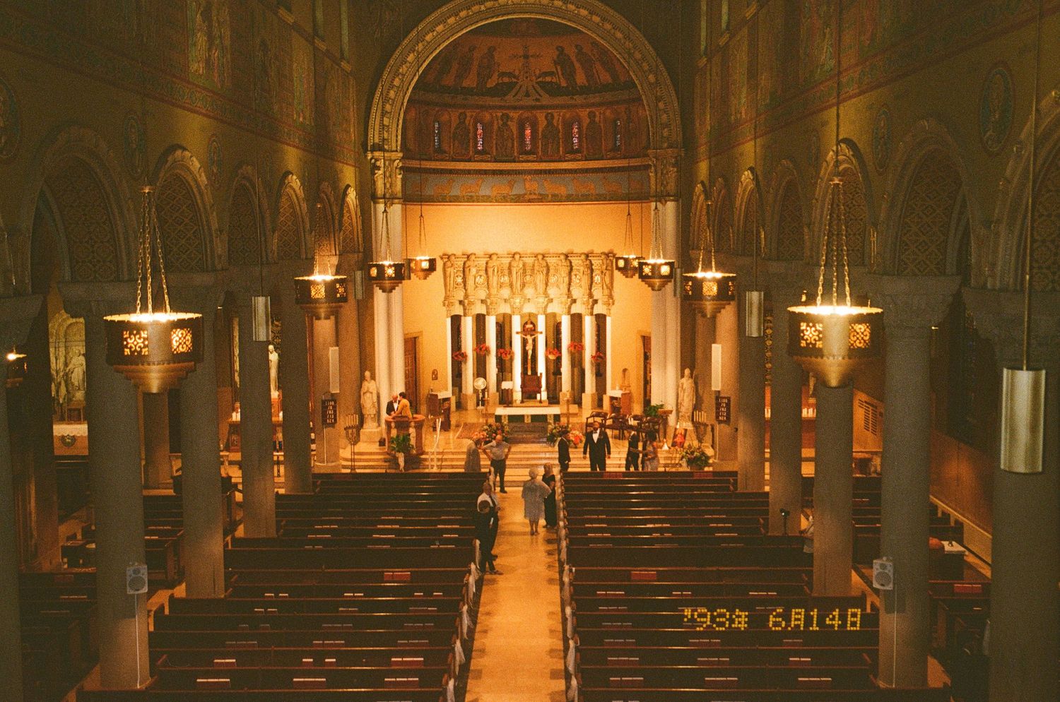 Interior view of a grand cathedral with warm lighting illuminating the altar, pews and ornate architectural details.